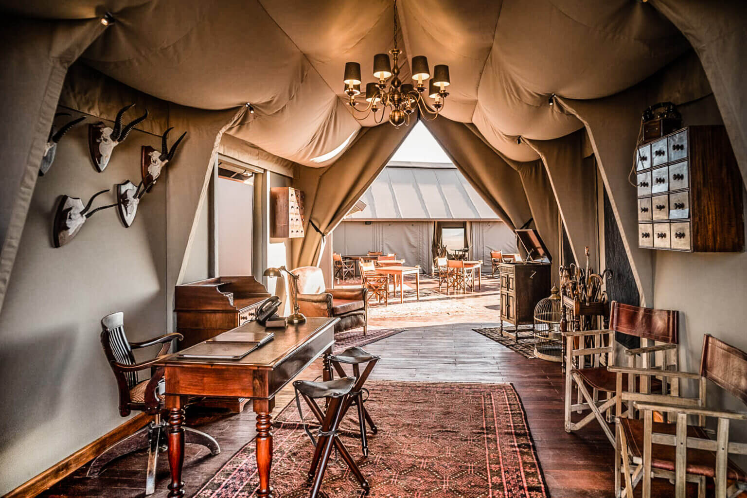 Zannier Sonop, Africa — Canvas bell tent interior with wooden desk, brass chandelier, animal mounts, and layered fabric ceiling opening to savanna landscape.