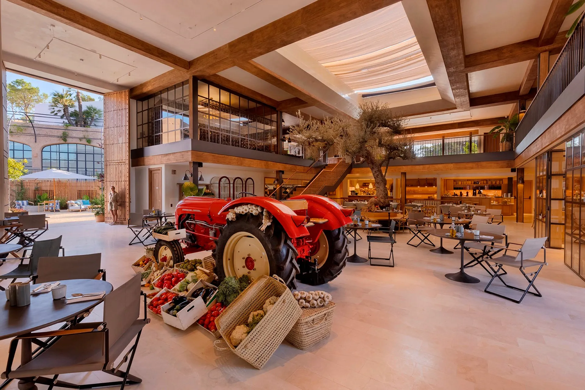 The Farmers Market, Balearic Islands, Spain — Red vintage tractor with fresh produce display in modern barn space with exposed wooden beams and skylights.