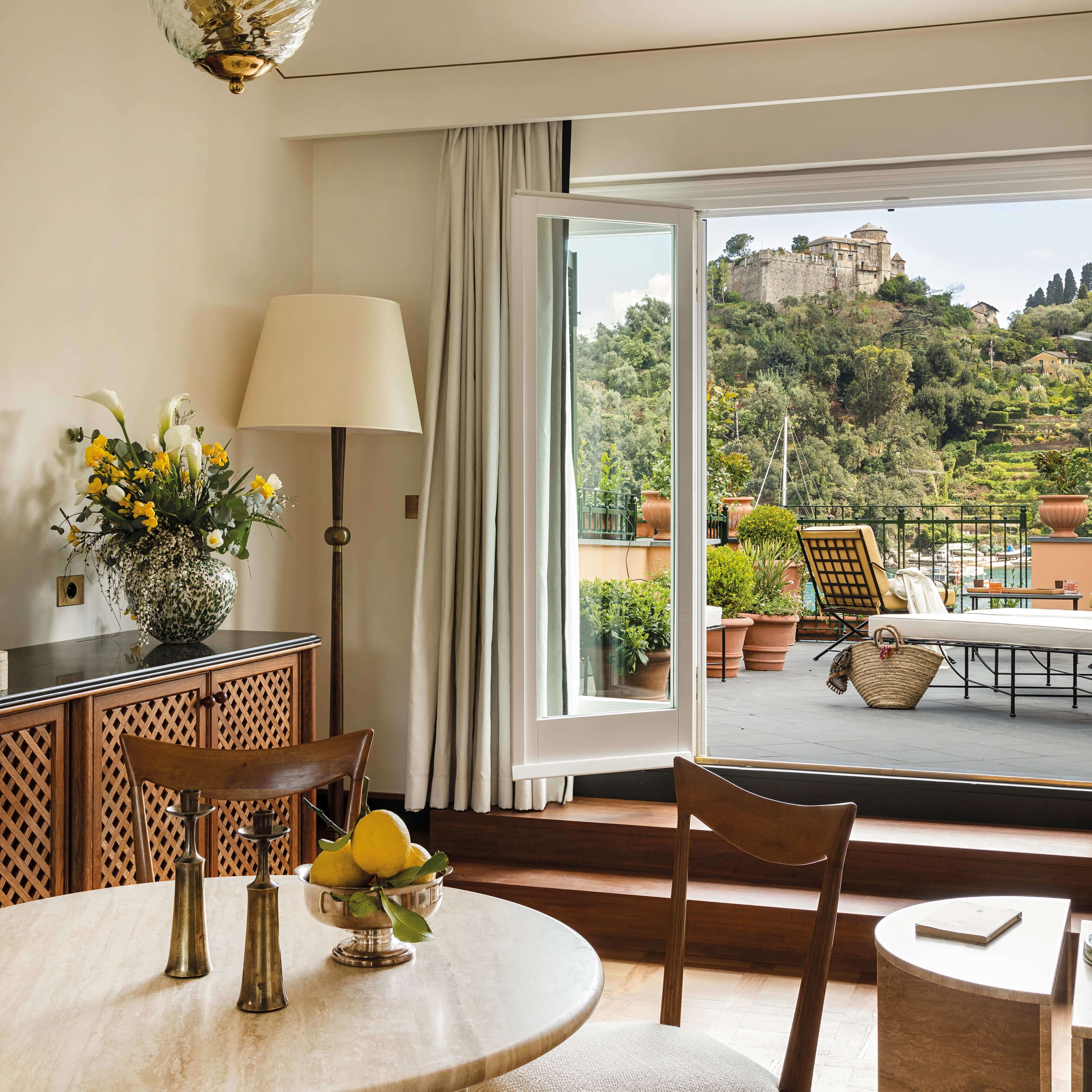 Splendido Mare, Europe — Sunlit bedroom with wooden furnishings, marble table, terracotta terrace, medieval hilltop castle views, warm neutral palette, luxury Italian Riviera aesthetic.