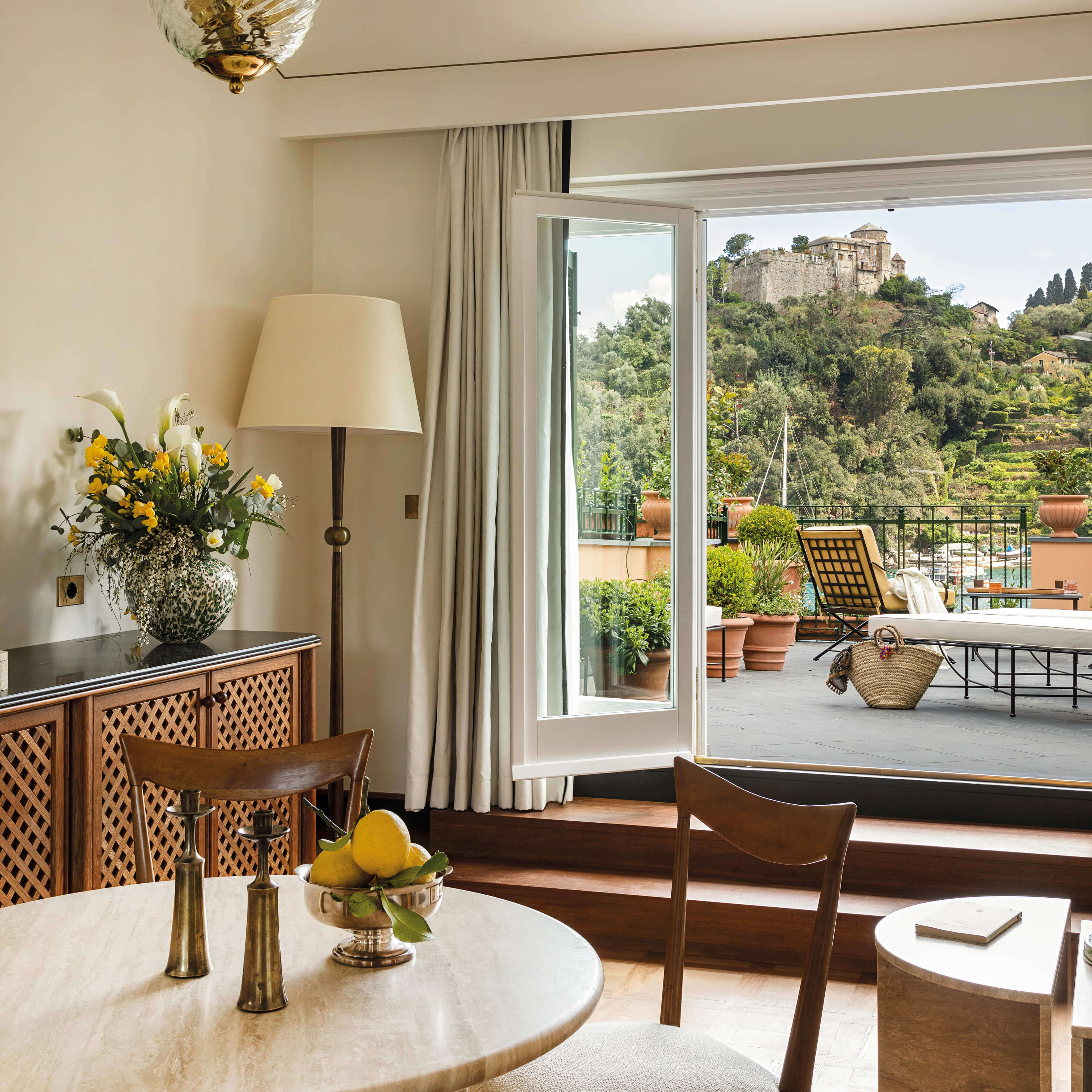 Splendido Mare, Europe — Sunlit bedroom with wooden furnishings, marble table, terracotta terrace, medieval hilltop castle views, warm neutral palette, luxury Italian Riviera aesthetic.
