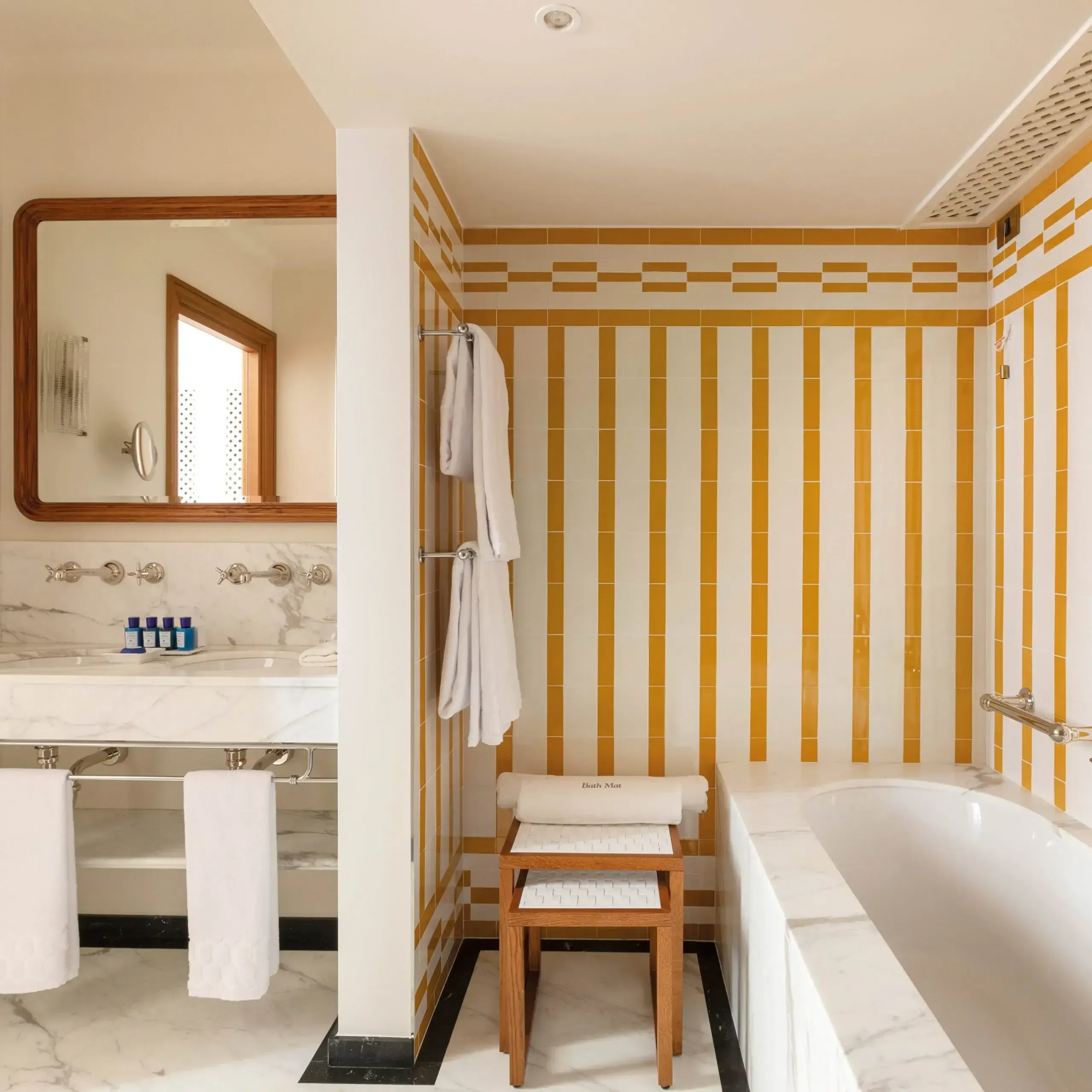 Splendido Mare, Europe — Marble bathroom with golden striped tile walls, white soaking tub, wooden stool, and dual vanity with mirror.