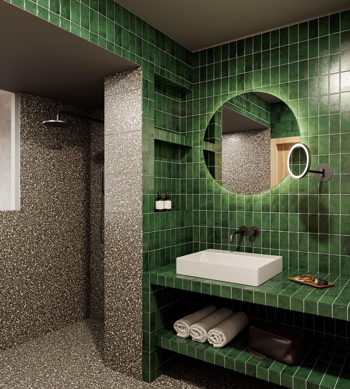 The Cōmodo — Cōmodo, Europe — Modern bathroom with forest-green vertical tile walls, terrazzo basin, arched mirror, open shelving, and walk-in shower with natural light.