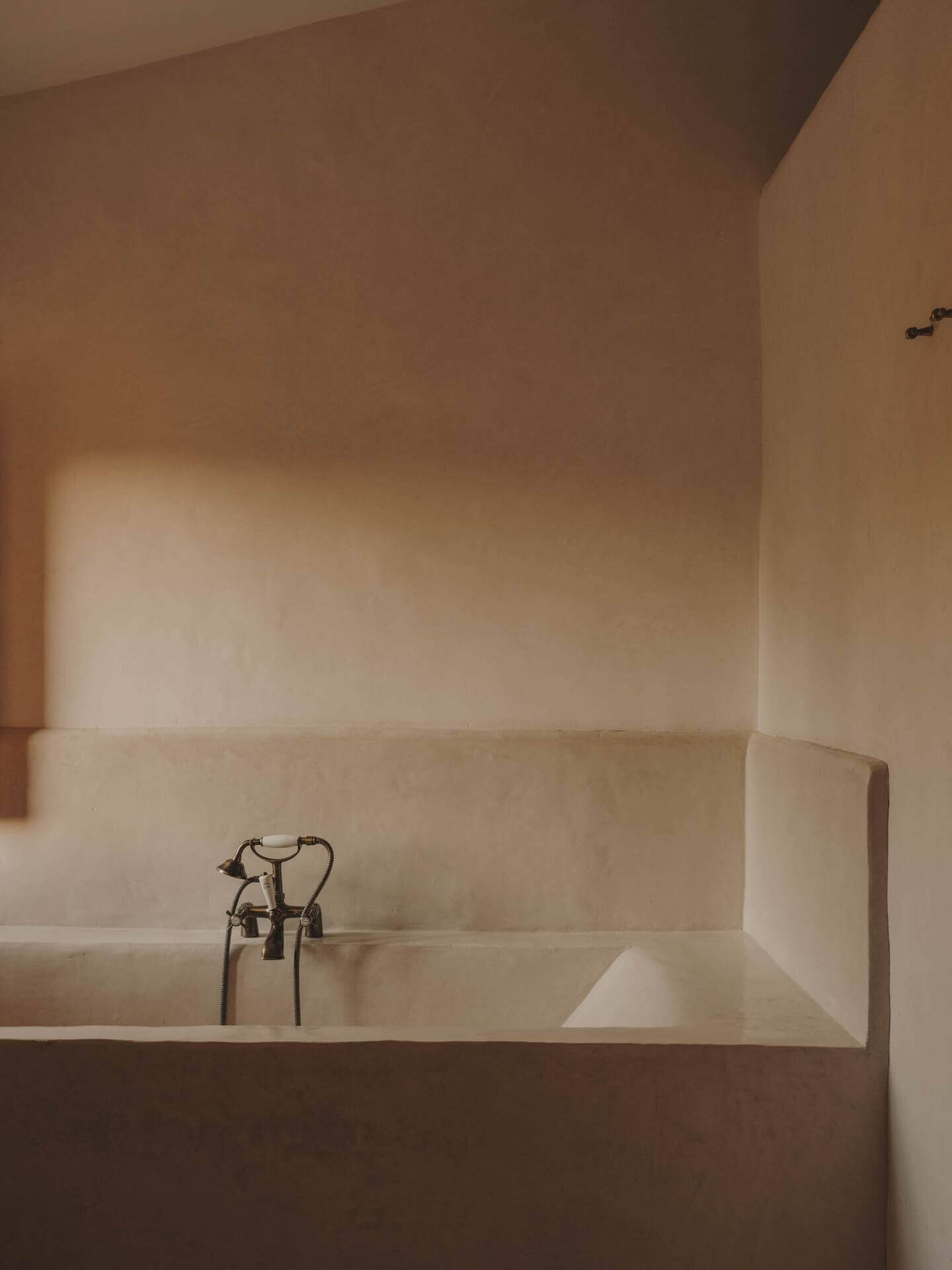 Can Lluïssó, Balearic Islands, Spain — Minimalist limestone bathtub with vintage brass fixtures, natural light, spa-like luxury bathroom architecture.