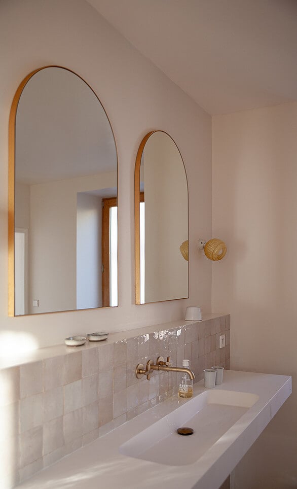 Casa Santa Teresa, Europe — Minimalist bathroom with arched oak mirrors, white subway tile backsplash, brass wall-mounted faucet, and soft natural light.