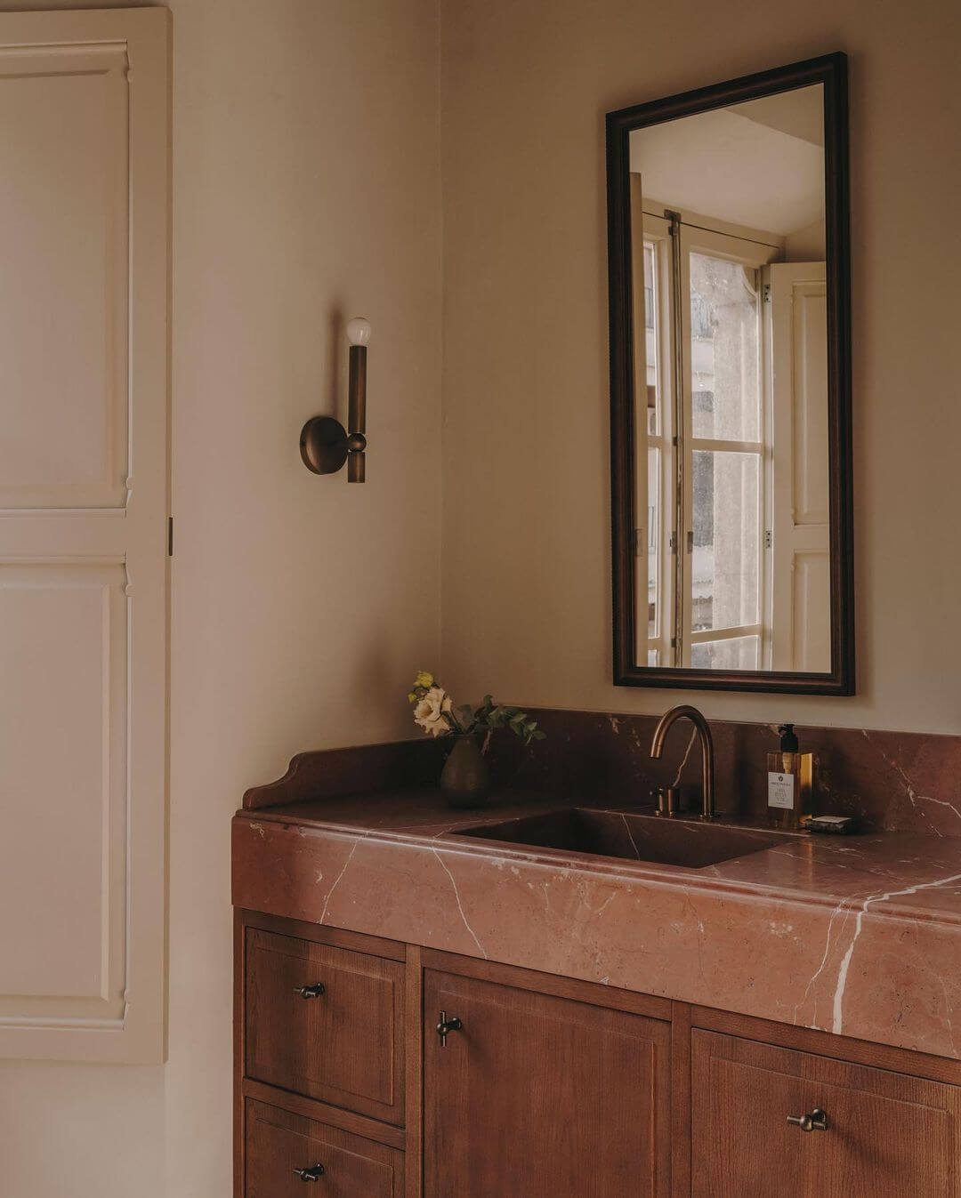 Santa Teresa 34, Balearic Islands — Terracotta marble vanity with wooden cabinetry, black-framed mirror, and minimalist sconce in warm-toned bathroom.