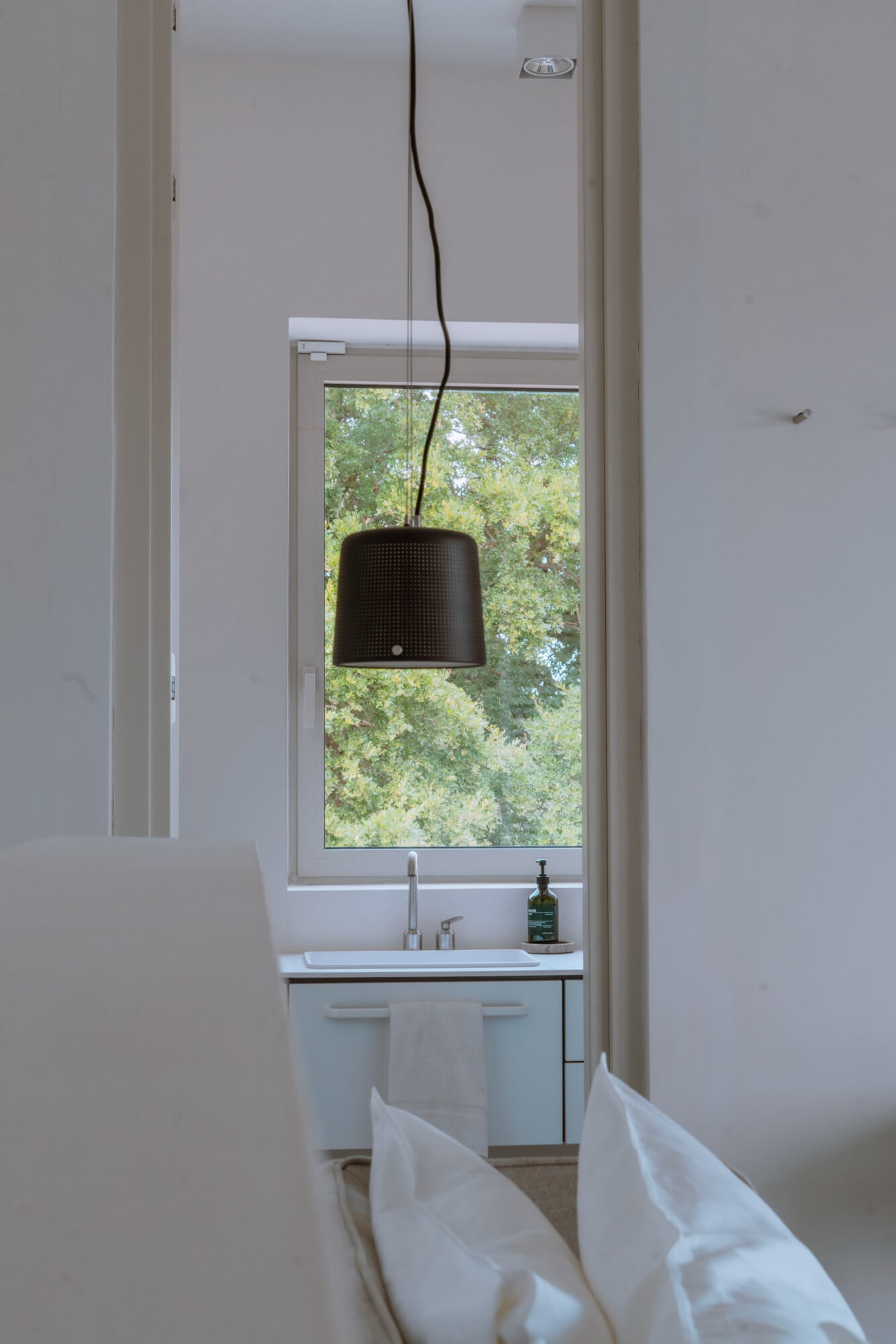 Villa Quercia, Italy — Minimalist bathroom with pendant lamp, white sink, tall window framing green trees, natural light, modern luxury interior design.