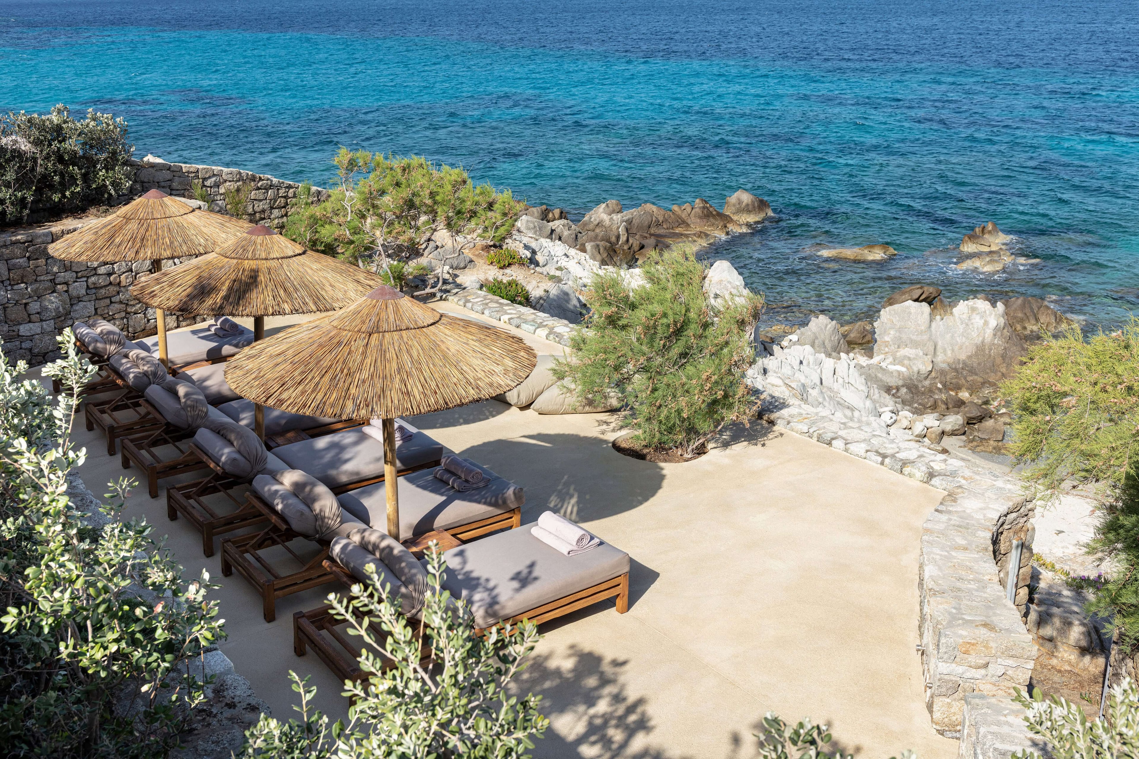 Villa Tama, Europe — Private beach cove with thatched umbrellas, loungers, natural stone terracing, turquoise sea, and Mediterranean landscape design.