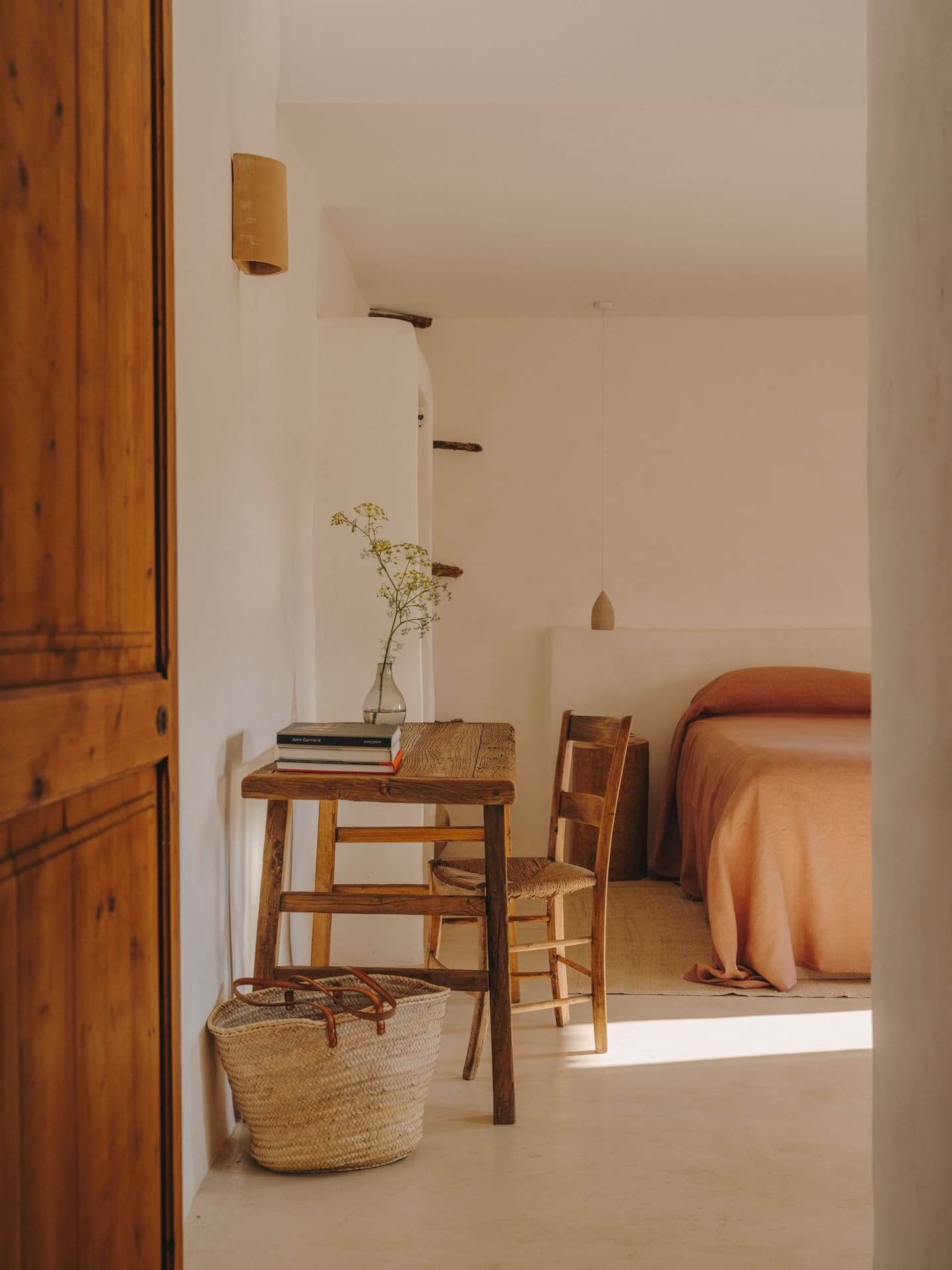 Can Lluïssó, Balearic Islands, Spain — Minimalist bedroom with wooden desk, woven basket, dried flowers, terracotta linens, and natural light from window.