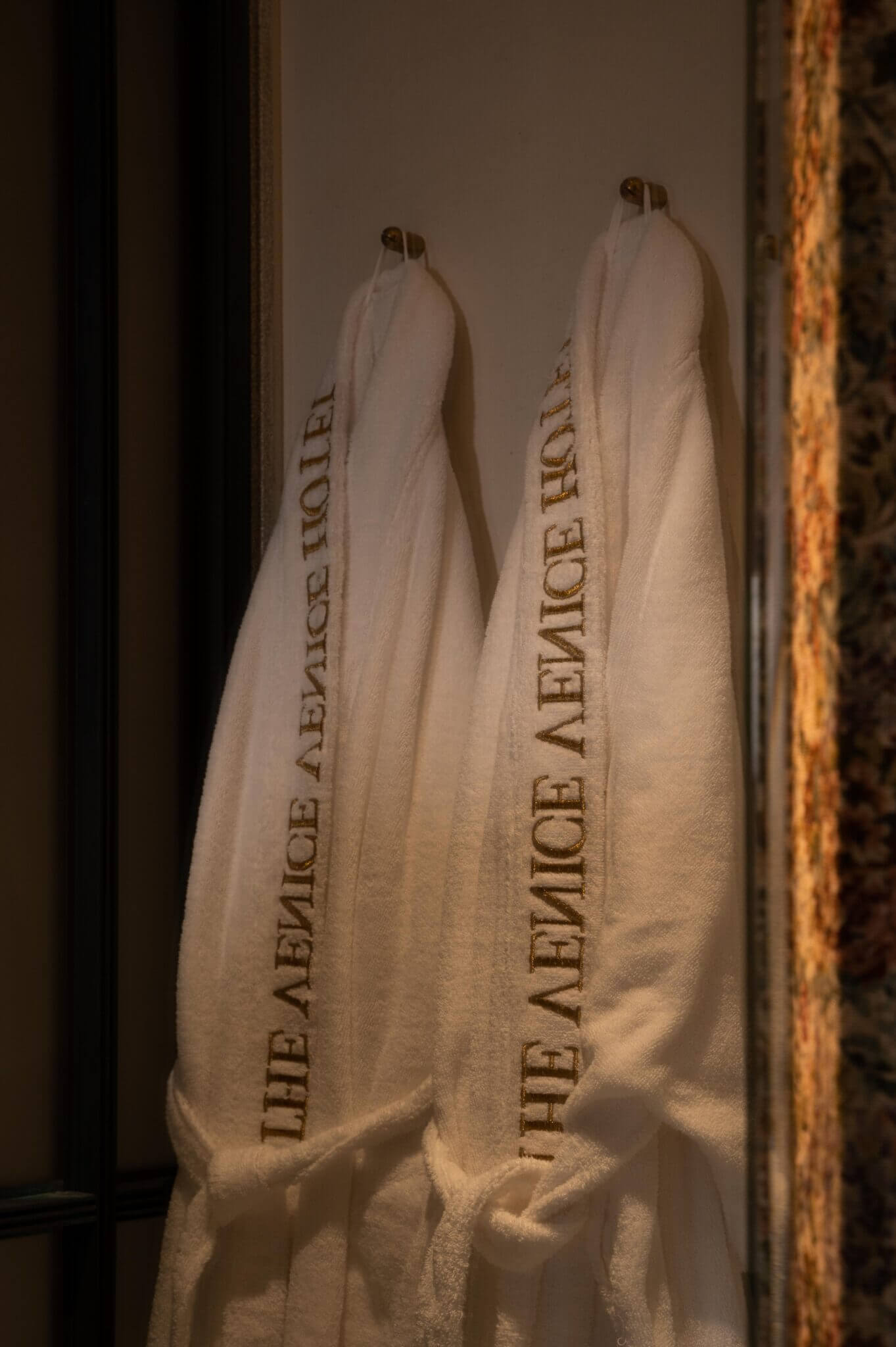 The Venice Venice Hotel, Venice, Italy — Cream linen towels embroidered with hotel name, hung on brass rings against warm architectural detail and ambient lighting.