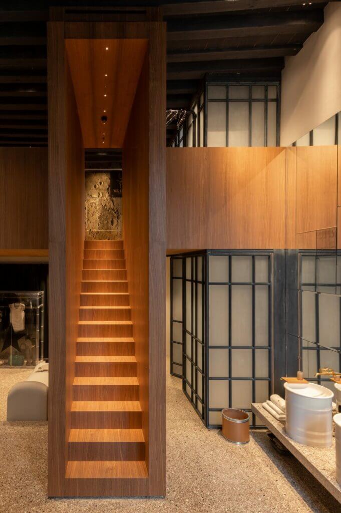 The Venice Venice Hotel, Europe — Wooden staircase with warm ambient lighting ascending to sculptural artwork in minimalist hotel corridor with glass partitions and concrete flooring.