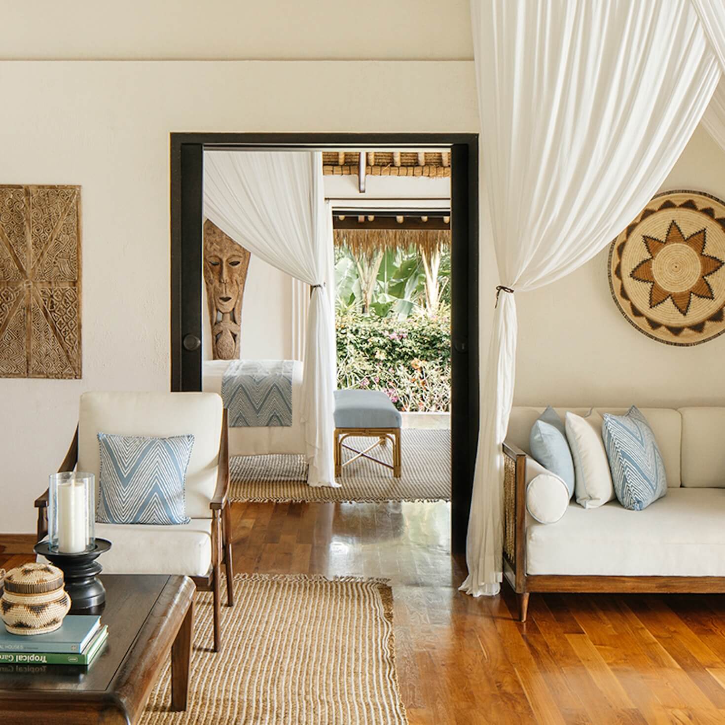 NIHI Sumba, Indonesia — Cream linen daybed with woven accents, sheer curtains, and carved wooden masks in serene tropical interior.