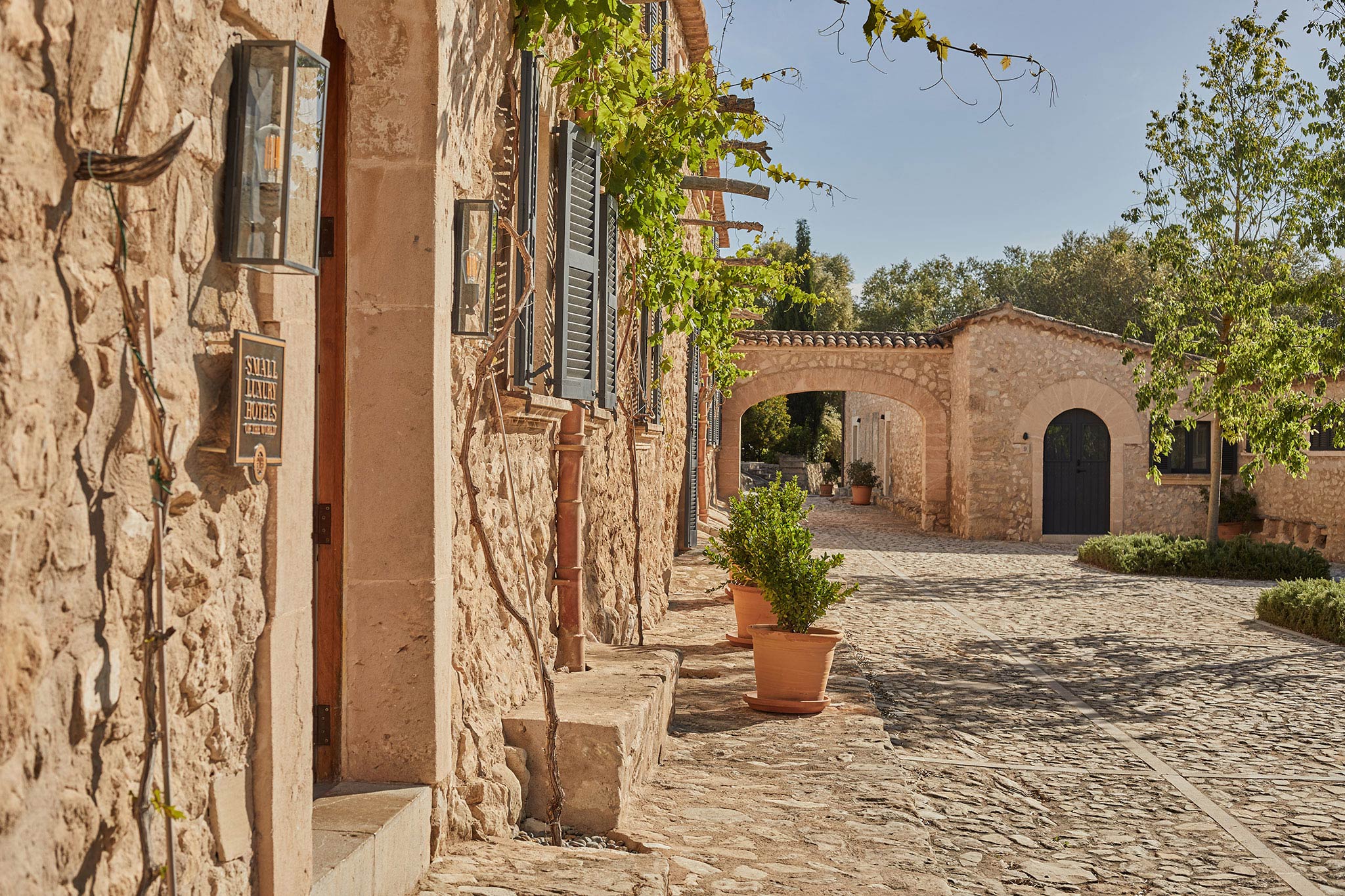 Finca Serena, Balearic Islands, Spain — Terracotta courtyard with stone archways, ivy-draped walls, and Mediterranean vernacular architecture in afternoon light.