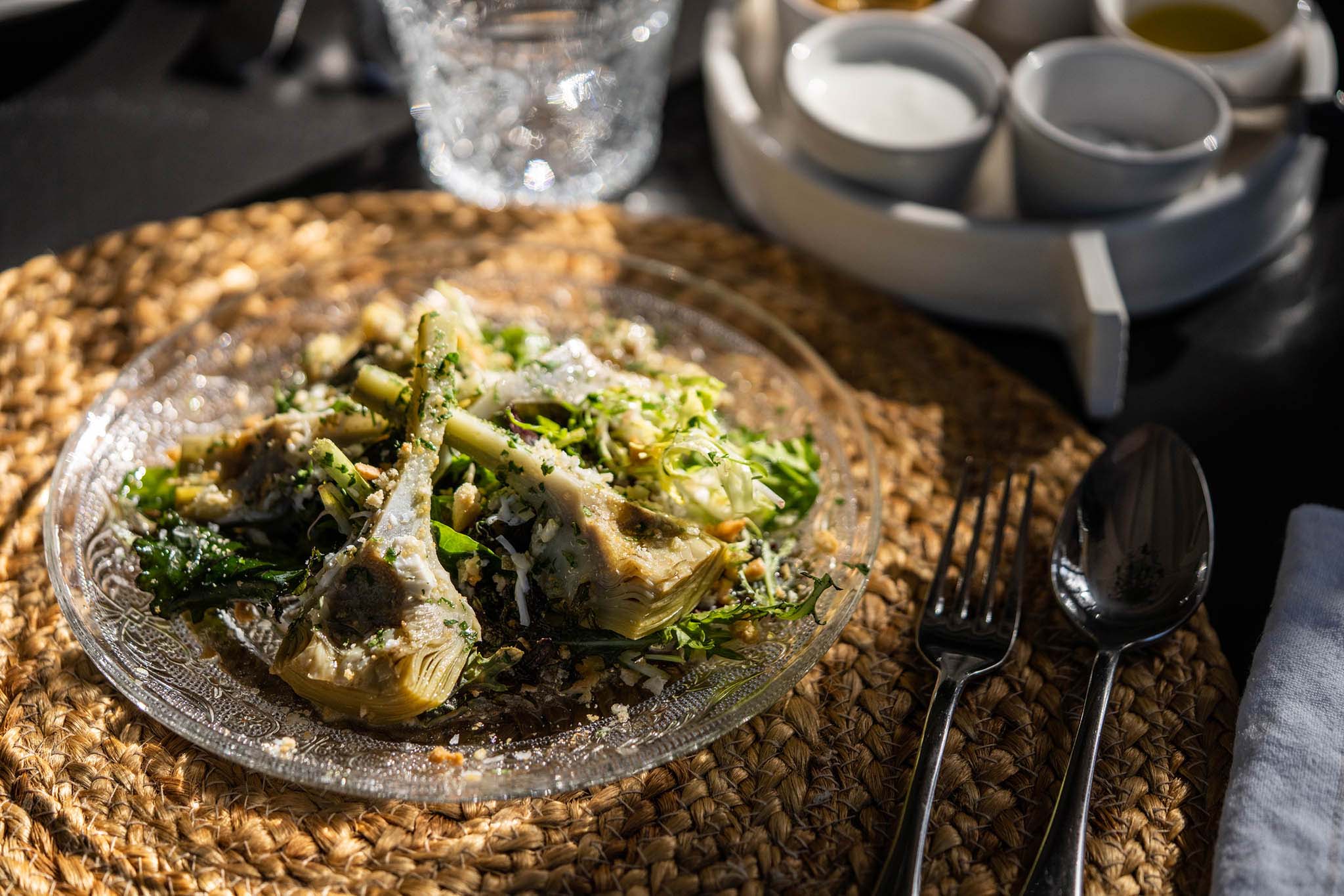 Jacaranda Restaurant, Balearic Islands — Grilled artichoke hearts with herbs and parmesan on textured glass plate, natural light, minimalist dining setup.