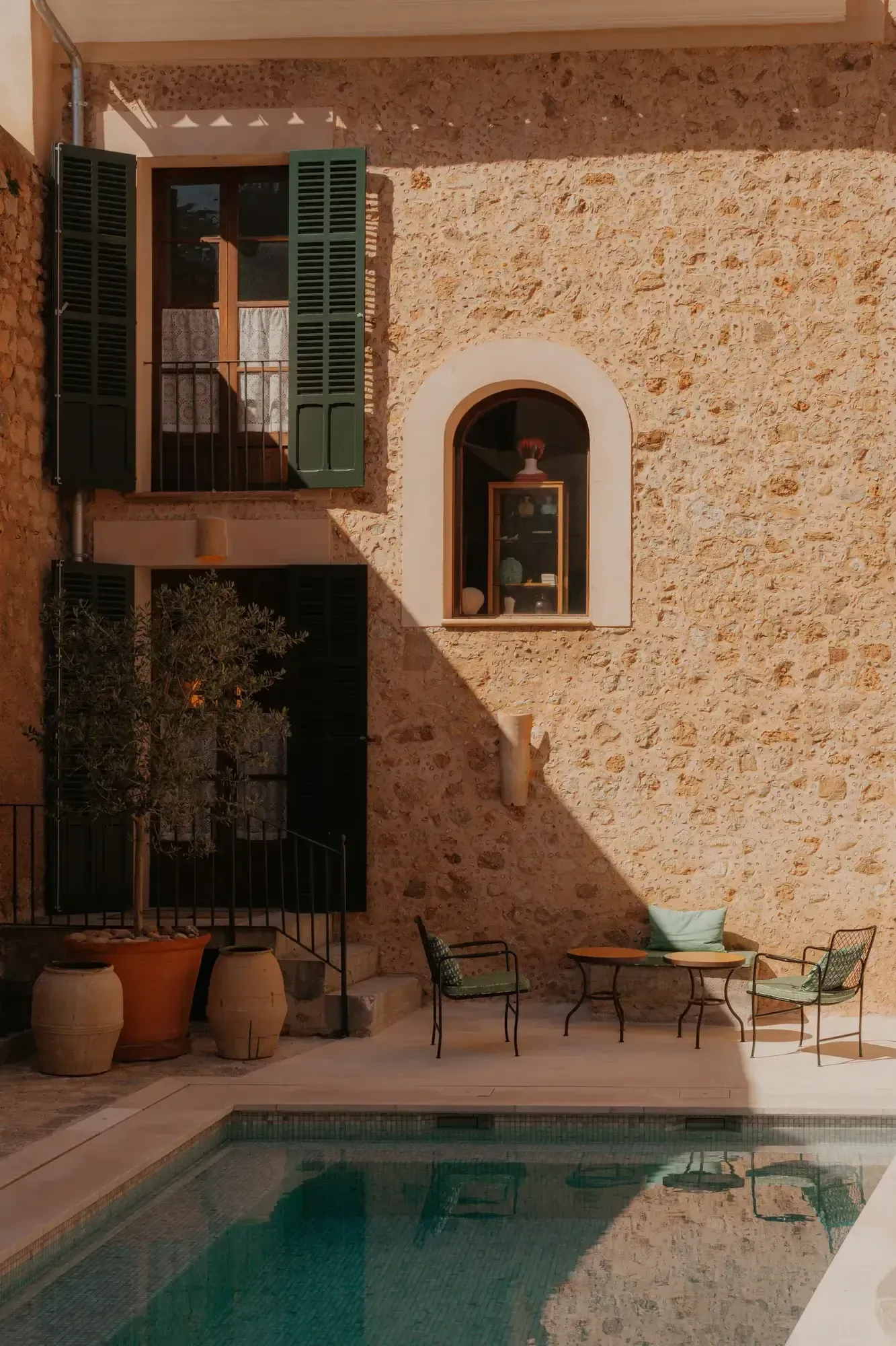 By Milagro: The team behind Mallorca's new wave of design stays — Mediterranean courtyard with stone walls, arched window, pool, and mid-century seating at luxury design hotel in Mallorca.