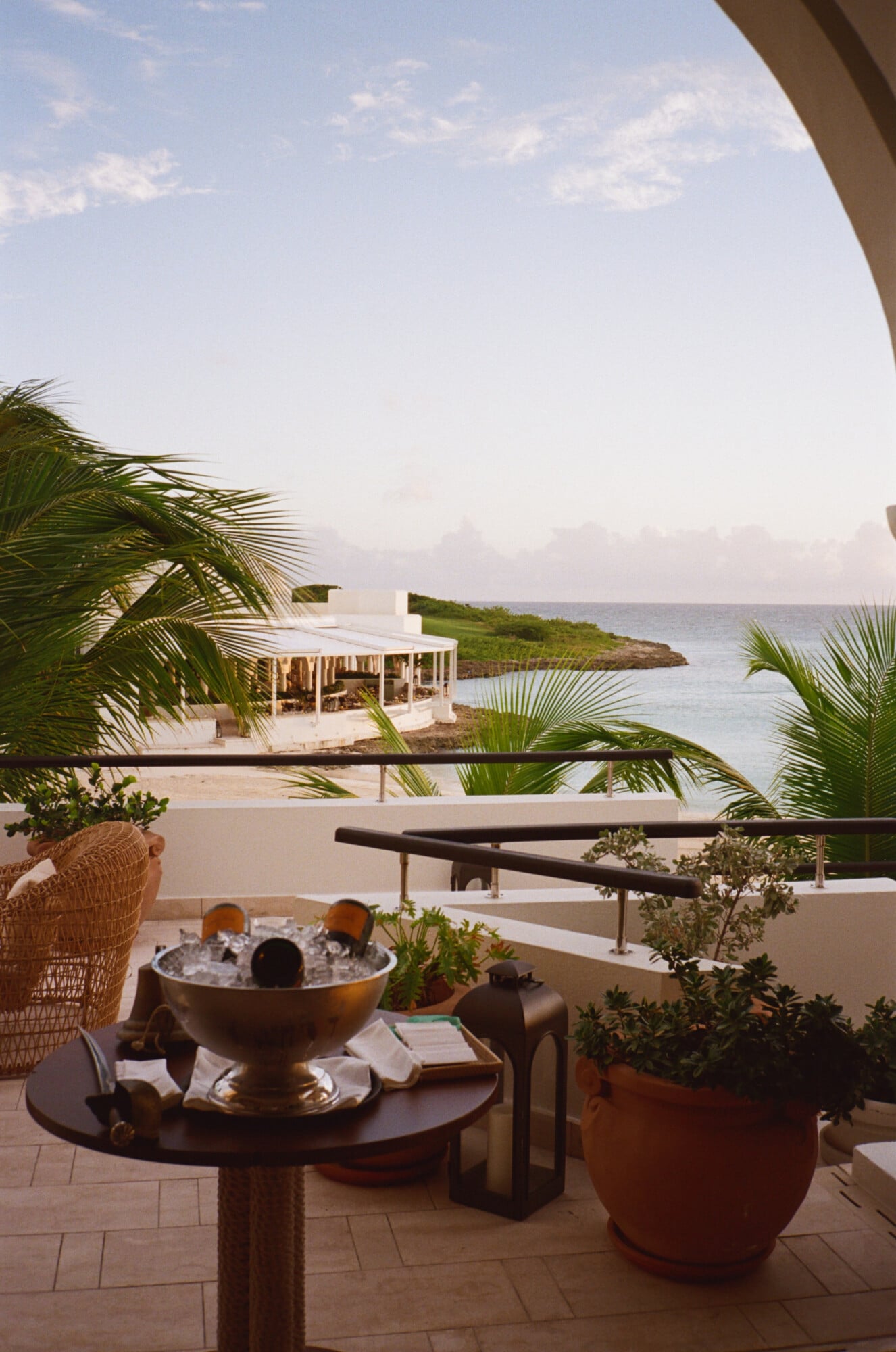 Sabering Ritual, North America — Coastal terrace with ice bucket, palm fronds, and minimalist pavilion overlooking calm turquoise waters and green peninsula.