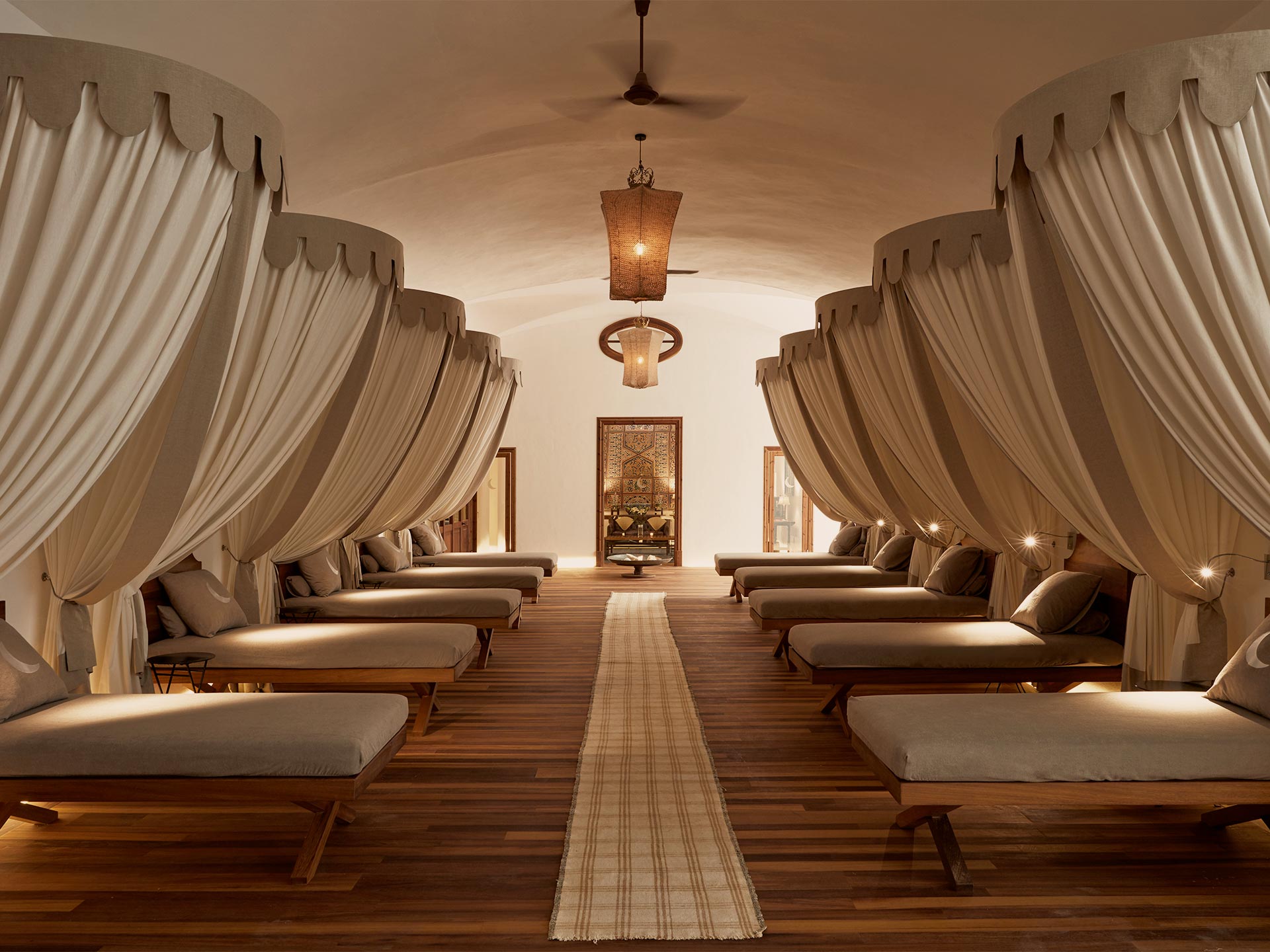 Cap Rocat Spa, Balearic Islands — Spa relaxation room with symmetrical daybed lounges, cream draped curtains, wooden flooring, and warm pendant lighting.