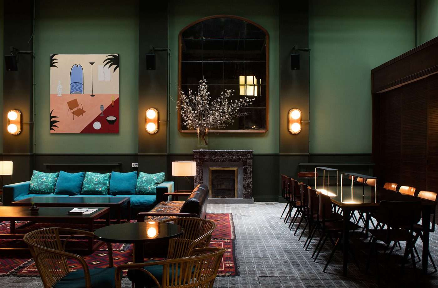 Casa Bonay, Barcelona, Spain — Mint-green gallery with turquoise sofa, fireplace, arched mirror, brass sconces, geometric rugs and contemporary artwork.