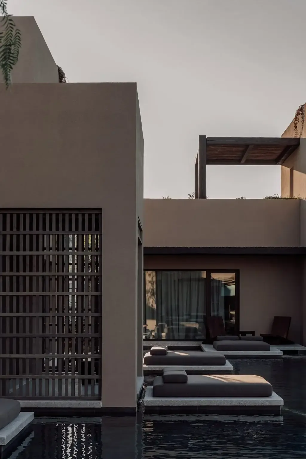 Casa Cook Samos, Greece — Minimalist poolside terrace with concrete architecture, dark loungers on platforms, wooden pergola, and earth-toned walls reflecting contemporary Mediterranean design.
