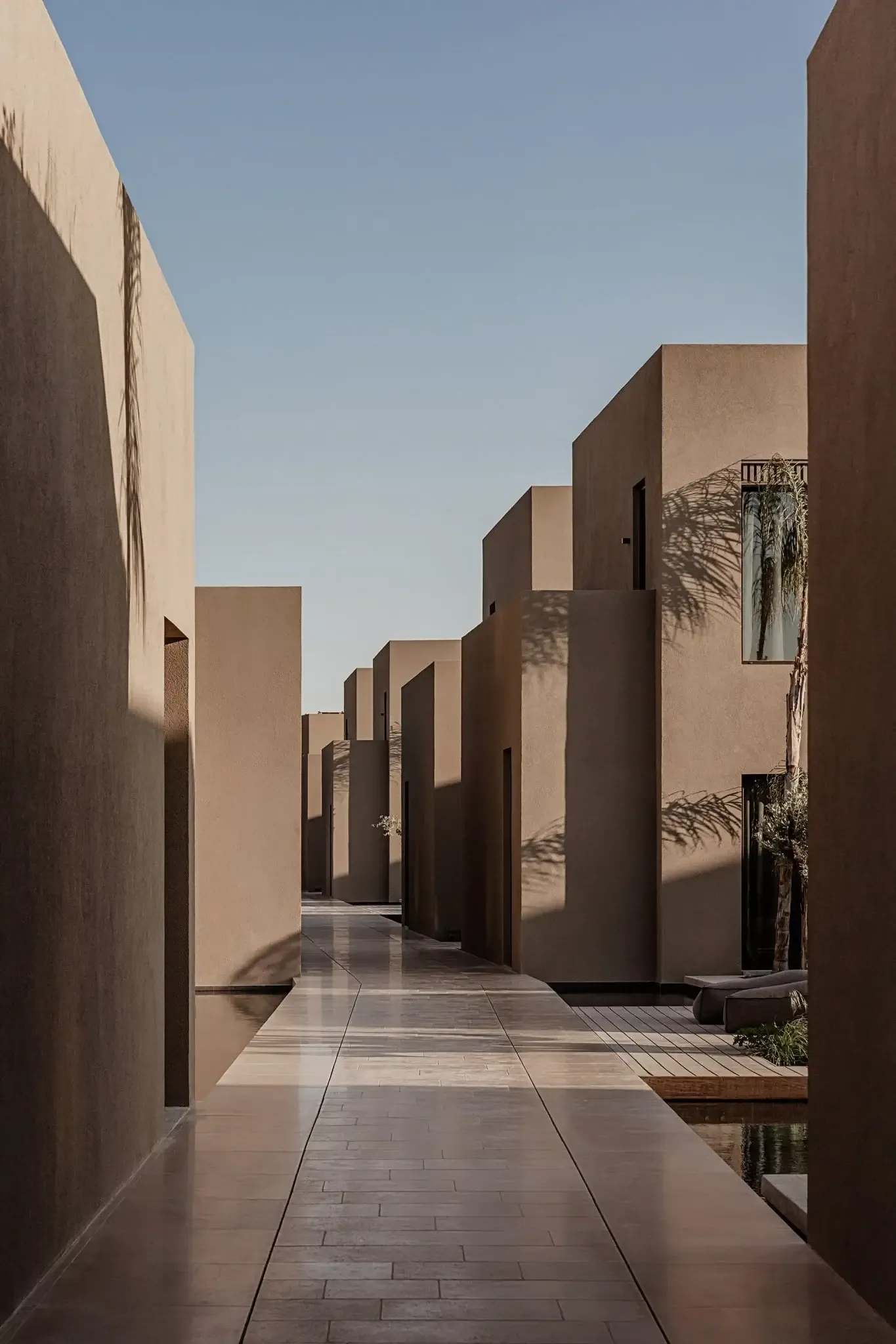 Casa Cook Samos, Greece — Minimalist concrete courtyard with geometric volumes, palm shadows, and polished stone pathway under clear sky.