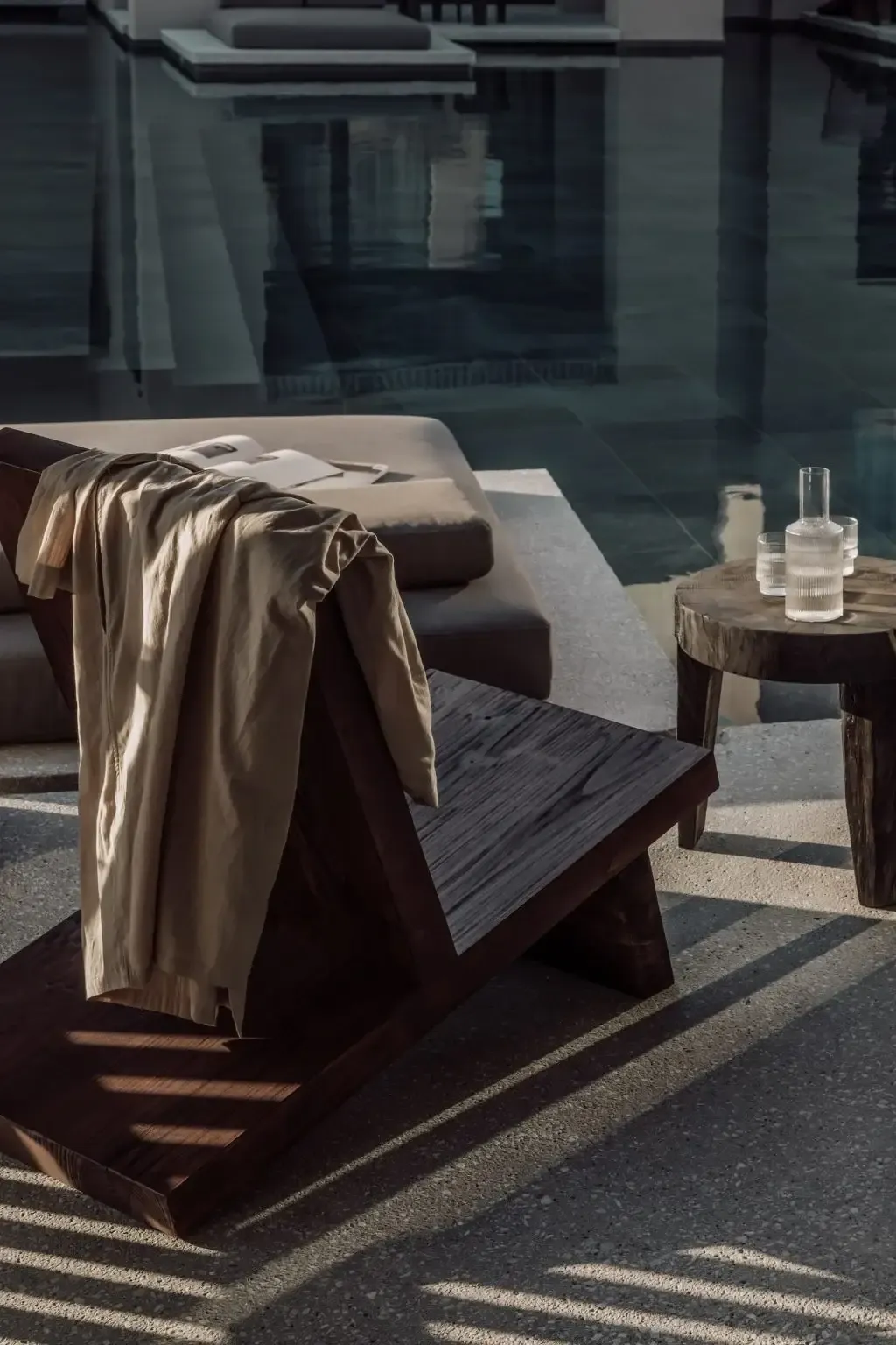 Casa Cook Samos, Greece — Dark wooden lounge chair with cream linen throw beside side table with glassware, concrete terrace with strong shadow patterns.