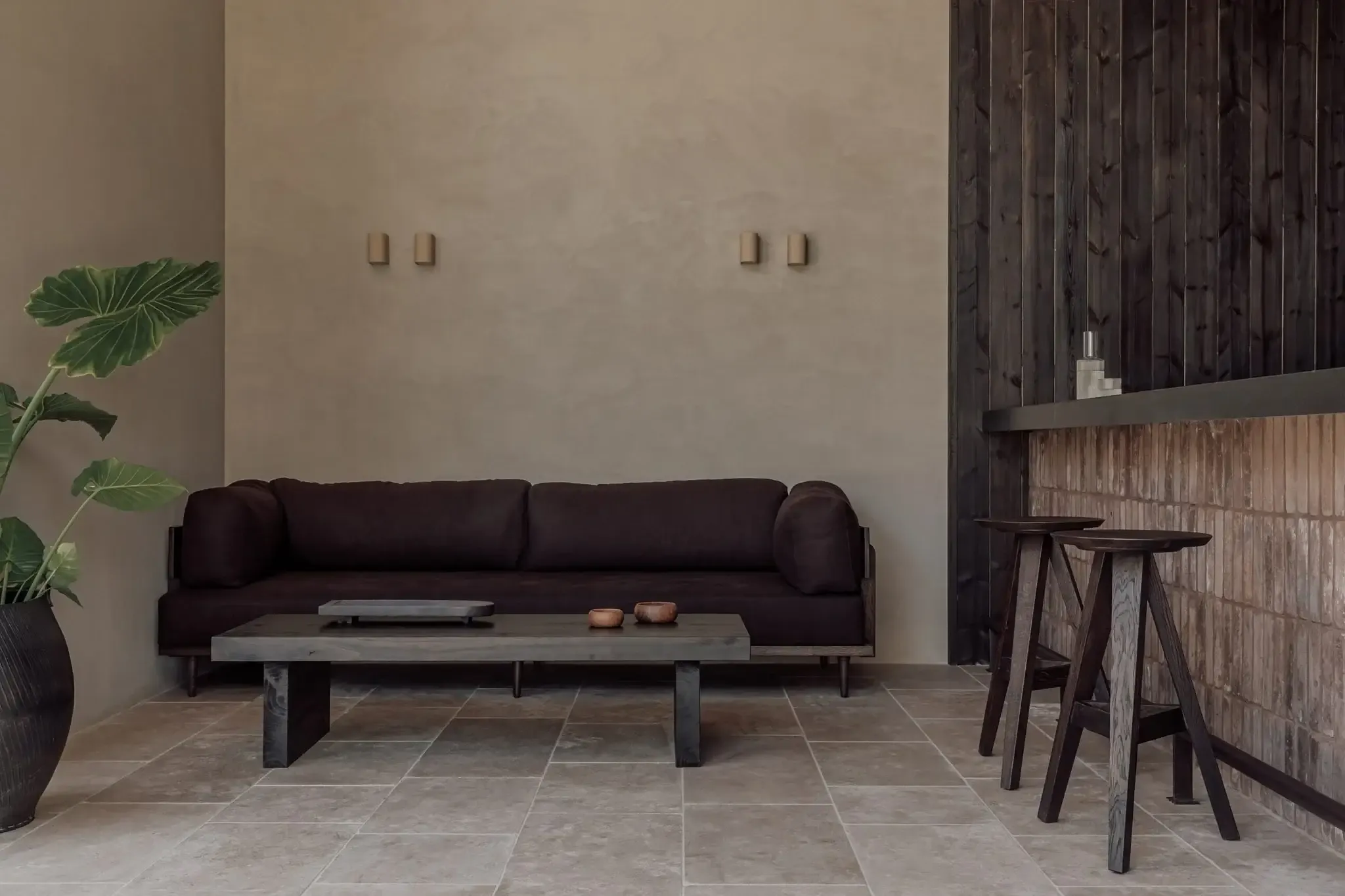 Casa Cook Samos, Greece — Dark sofa and concrete coffee table on stone flooring with wooden bar seating, minimalist interior design.
