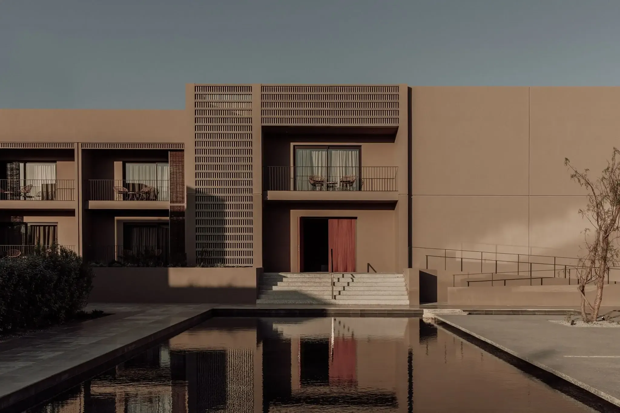 Casa Cook Samos, Greece — Minimalist terracotta facade with geometric brick screens, reflecting pool, and stepped entrance at golden hour.