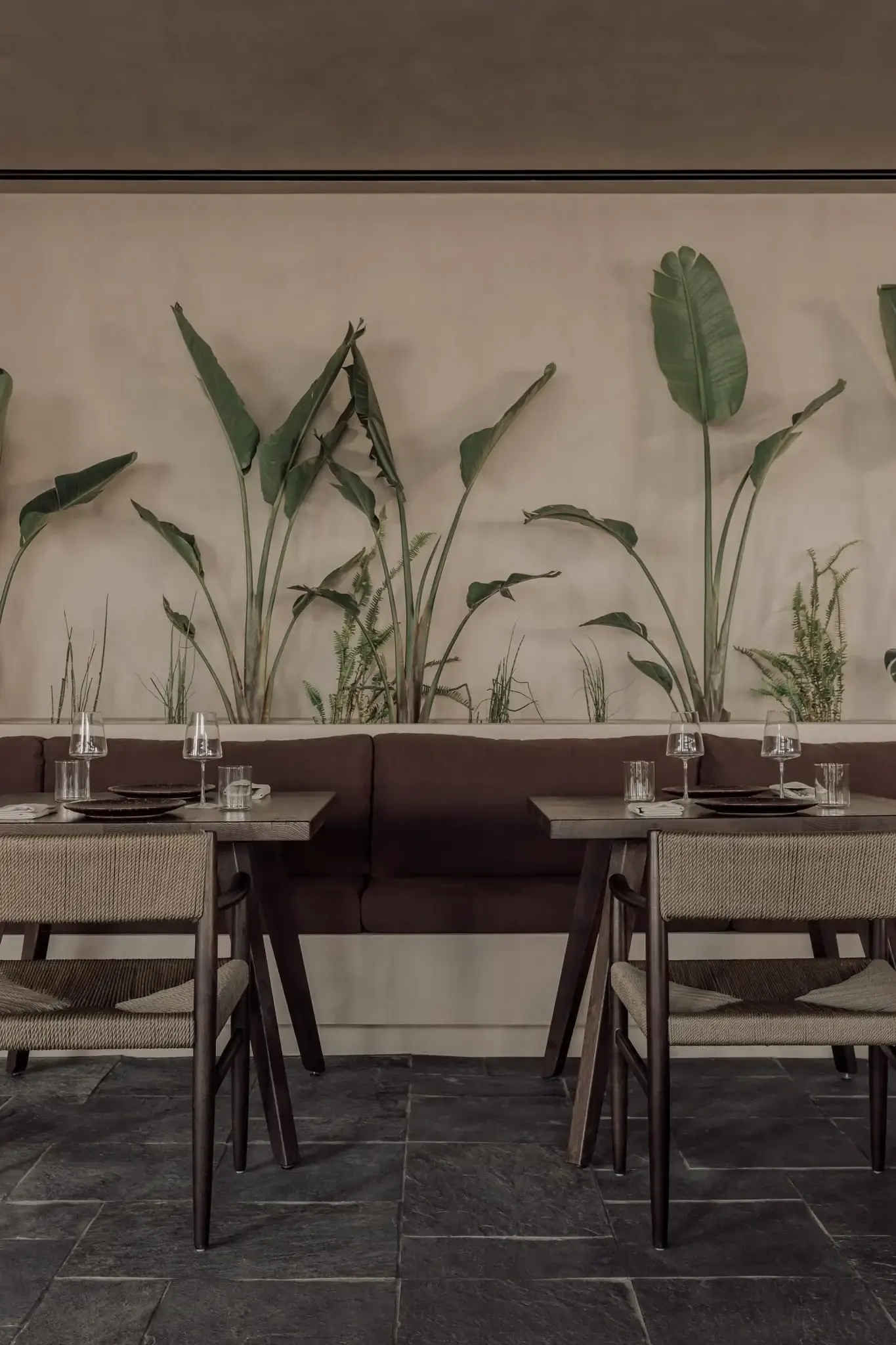 Casa Cook Samos, Europe — Dining area with dark wood chairs, burgundy banquette seating, botanical wall mural, water glasses, and slate flooring in minimalist restaurant interior.