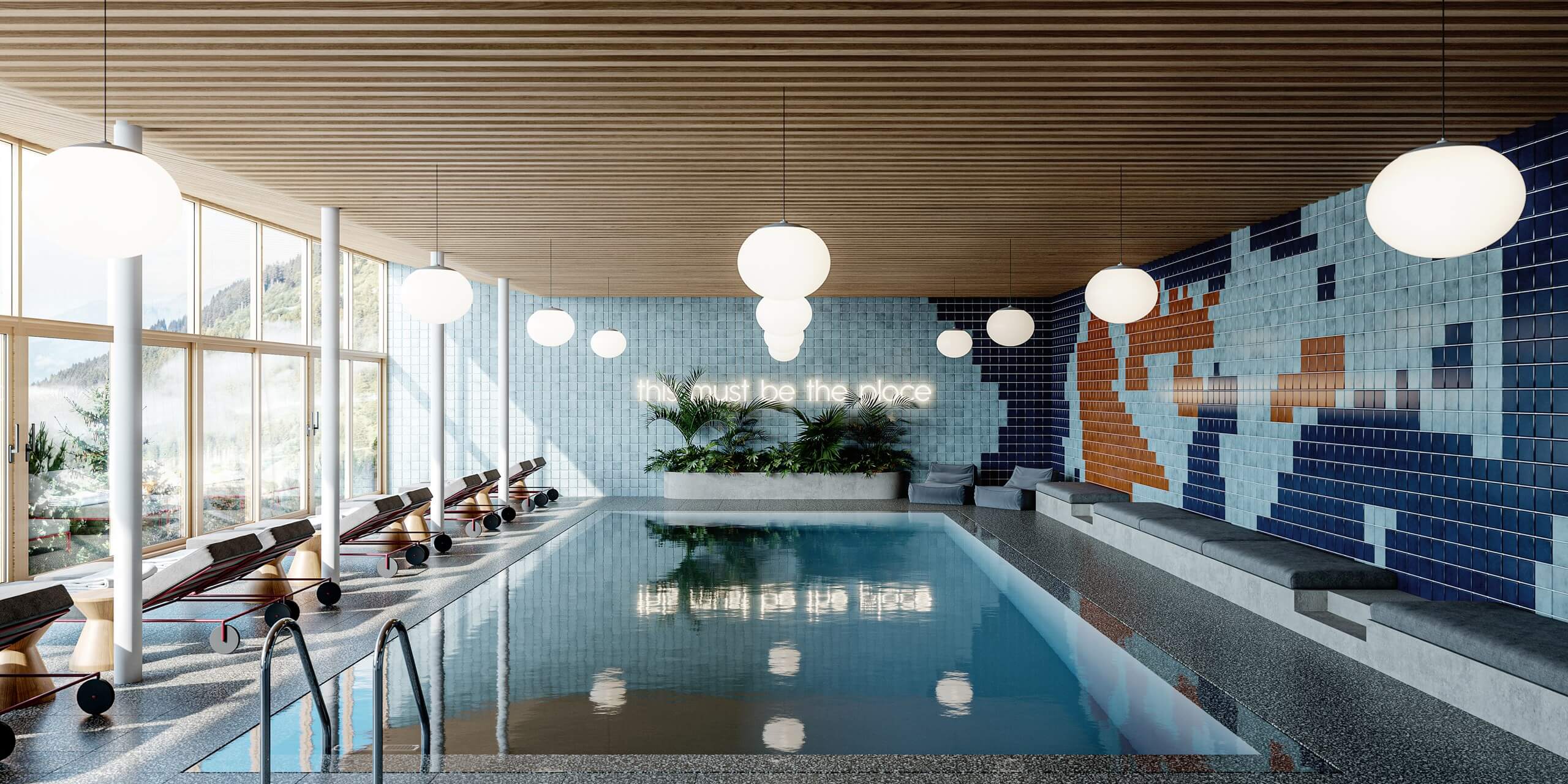 The Cōmodo — Cōmodo, Europe — Indoor swimming pool with light-filled glass facades, suspended cloud-form lighting, geometric tile mural, and lounge chairs overlooking forested landscape.