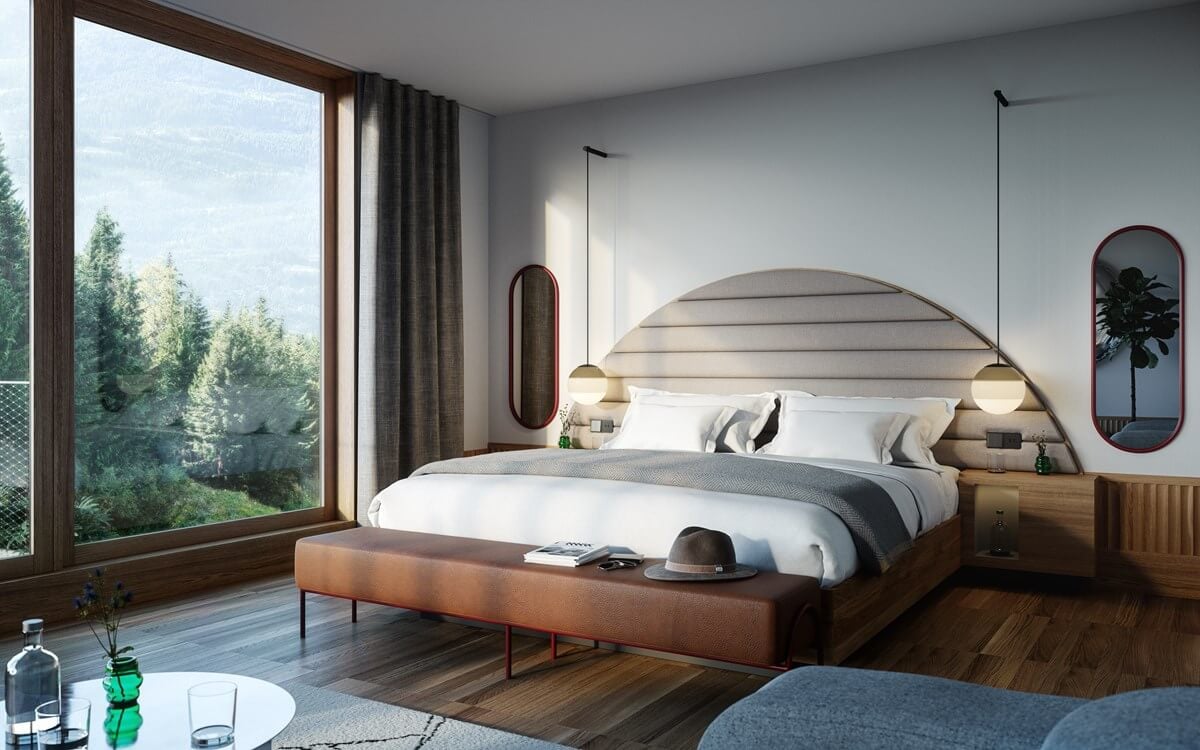 The Cōmodo — Cōmodo, Europe — Modern luxury bedroom with curved upholstered headboard, pendant lighting, wooden nightstands, leather bench, floor-to-ceiling windows overlooking forest, warm minimalist design.