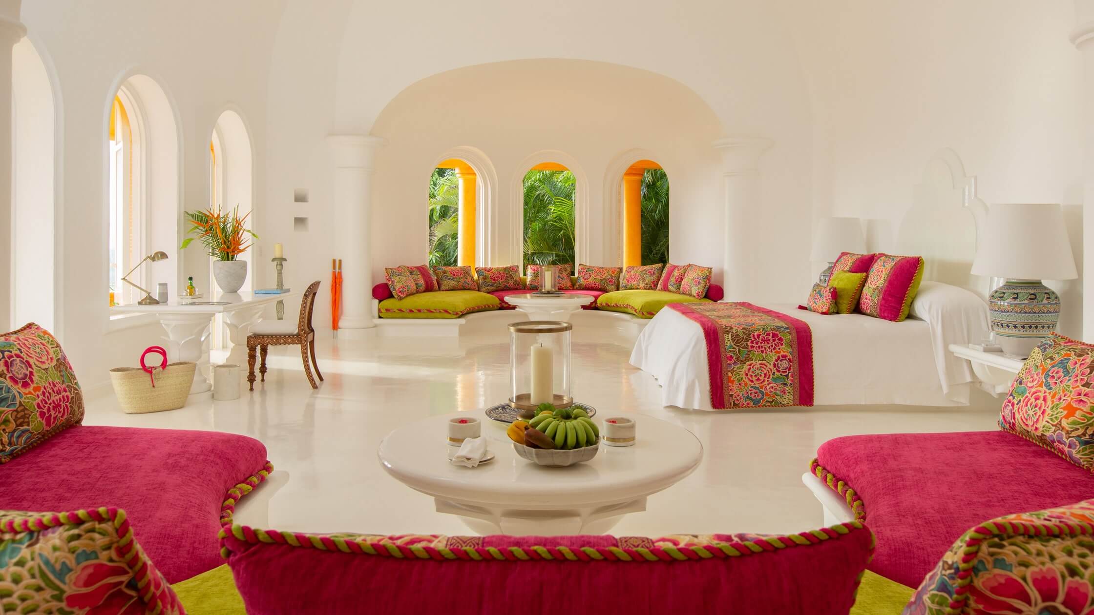 Cuixmala, Mexico — Whitewashed vaulted lounge with arched windows, fuchsia velvet seating, chartreuse cushions, ornamental textiles, central round table with fresh fruit, natural light through arches.