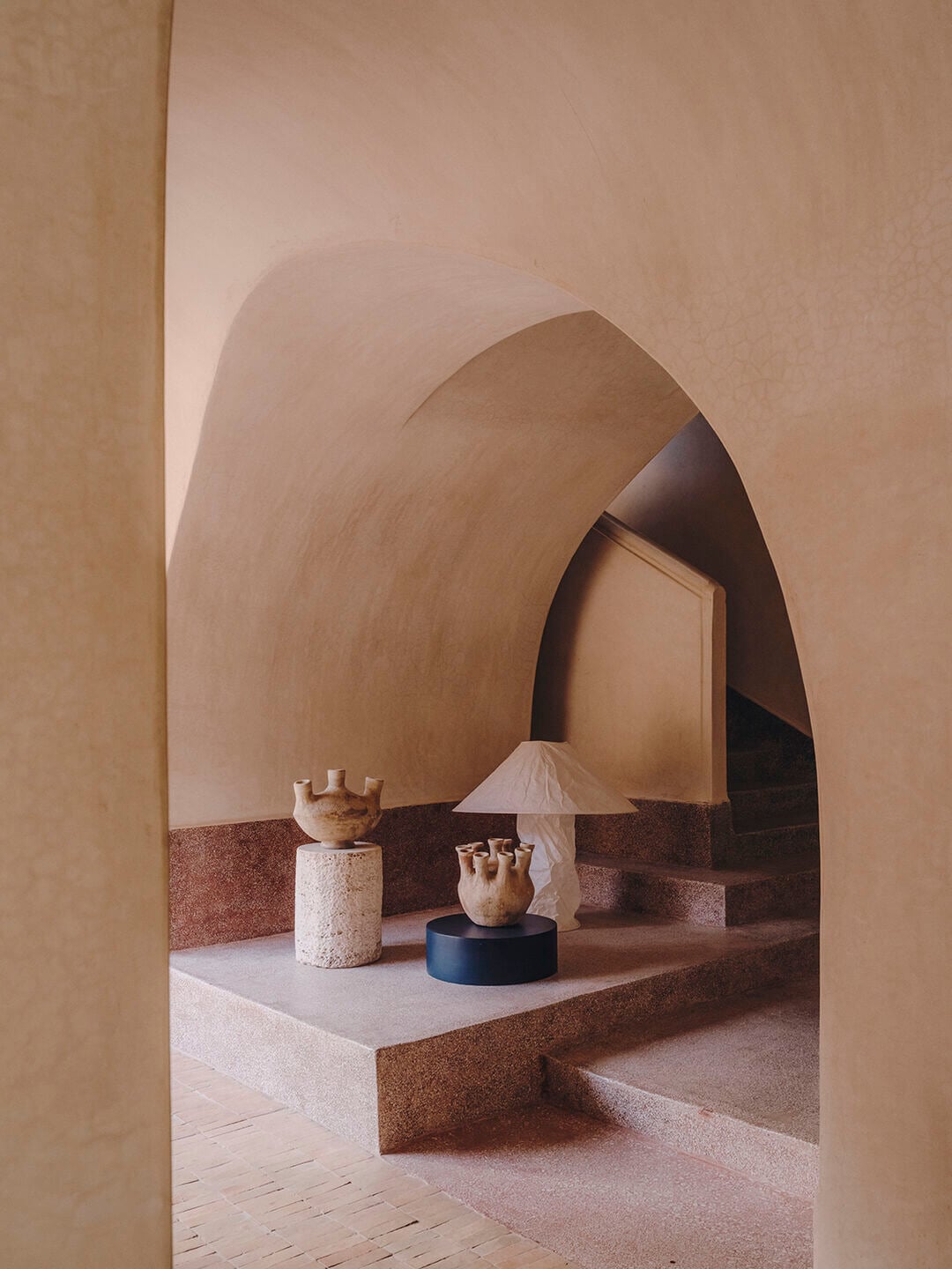 Maison Brummell Majorelle, Africa — Arched terracotta corridor with sculptural pottery vessels on stone plinth, warm earth-tone modernist architecture.