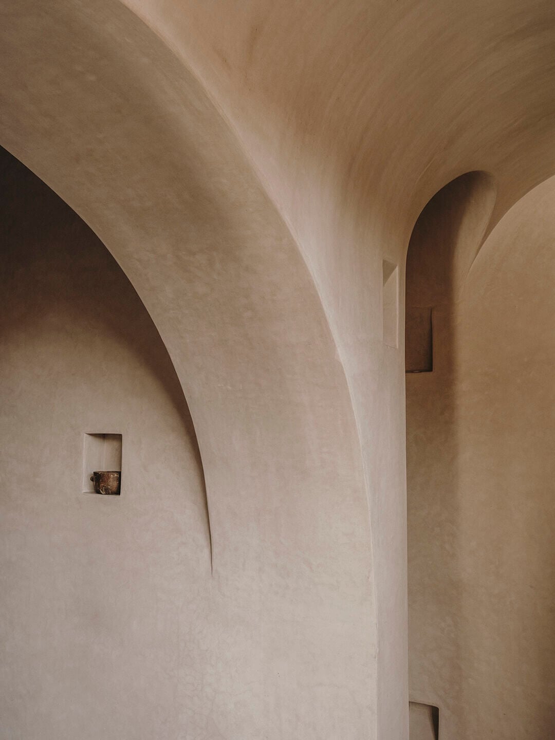 Maison Brummell Majorelle, Africa — Arched plaster walls with recessed niches and soft natural light creating sculptural shadows in minimalist corridor.