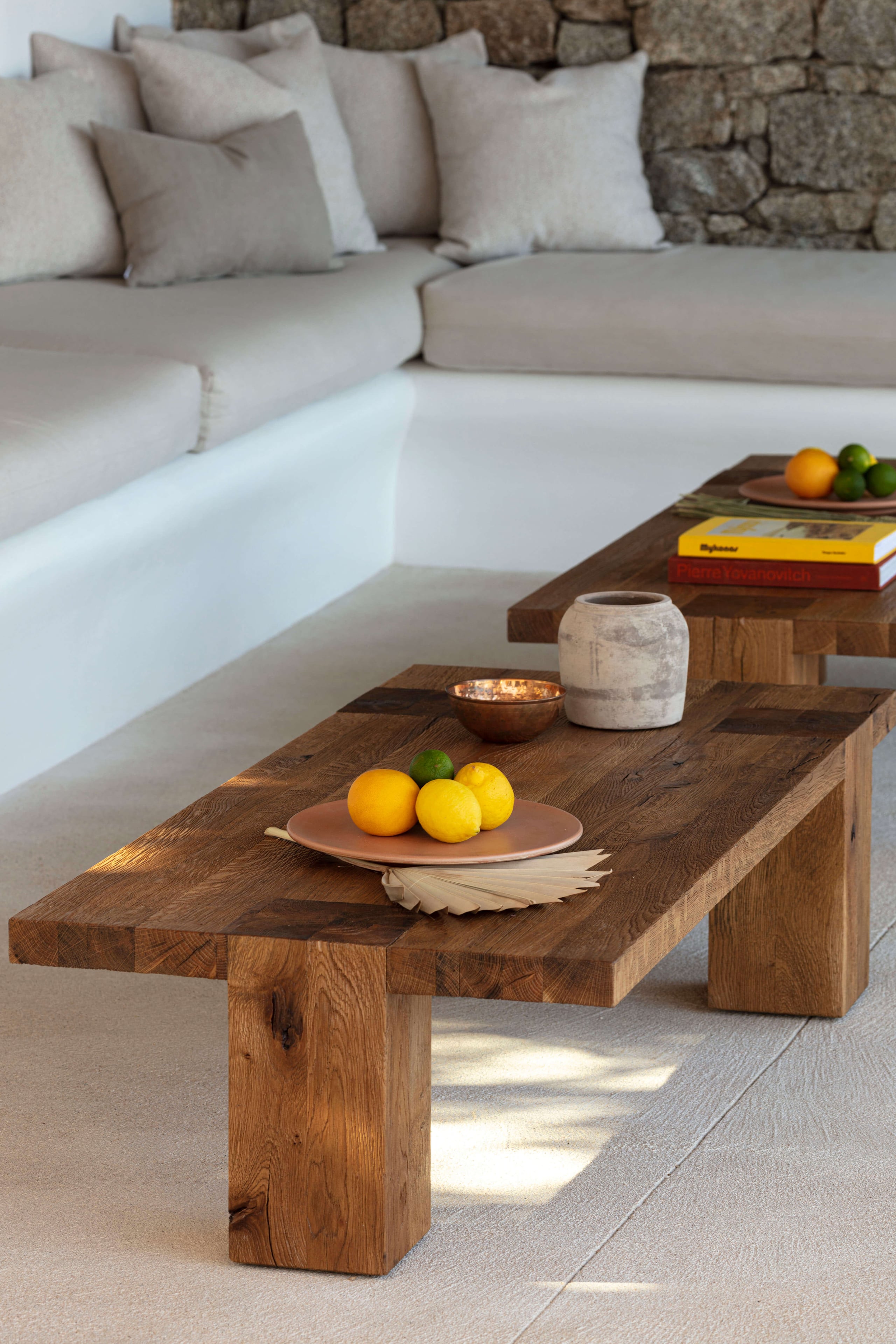 Villa Tama, Europe — Recessed seating area with cream linen sofa, raw wood coffee table, terracotta tableware, and stone fireplace in minimalist luxury interior.