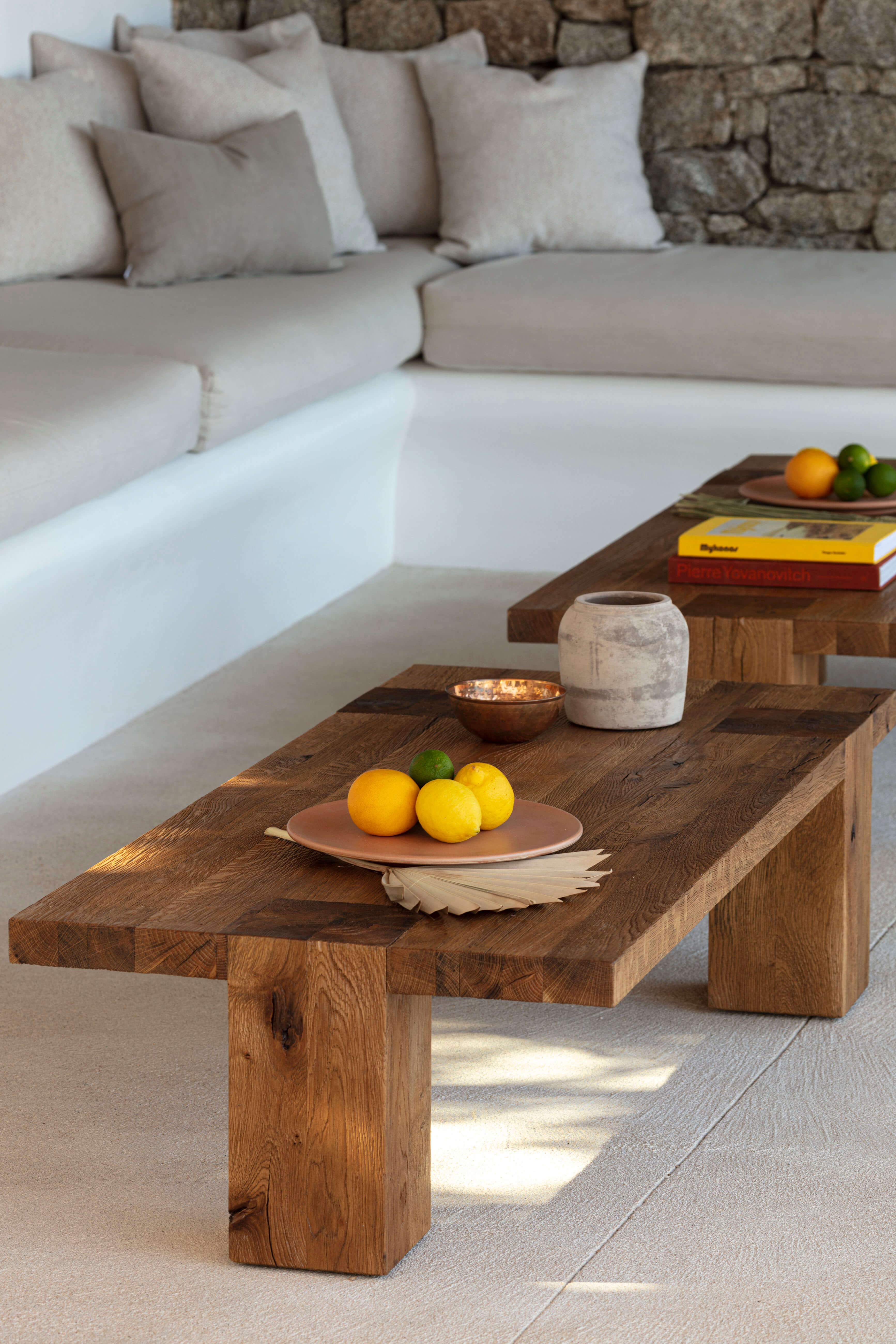 Villa Tama, Europe — Recessed seating area with cream linen sofa, raw wood coffee table, terracotta tableware, and stone fireplace in minimalist luxury interior.