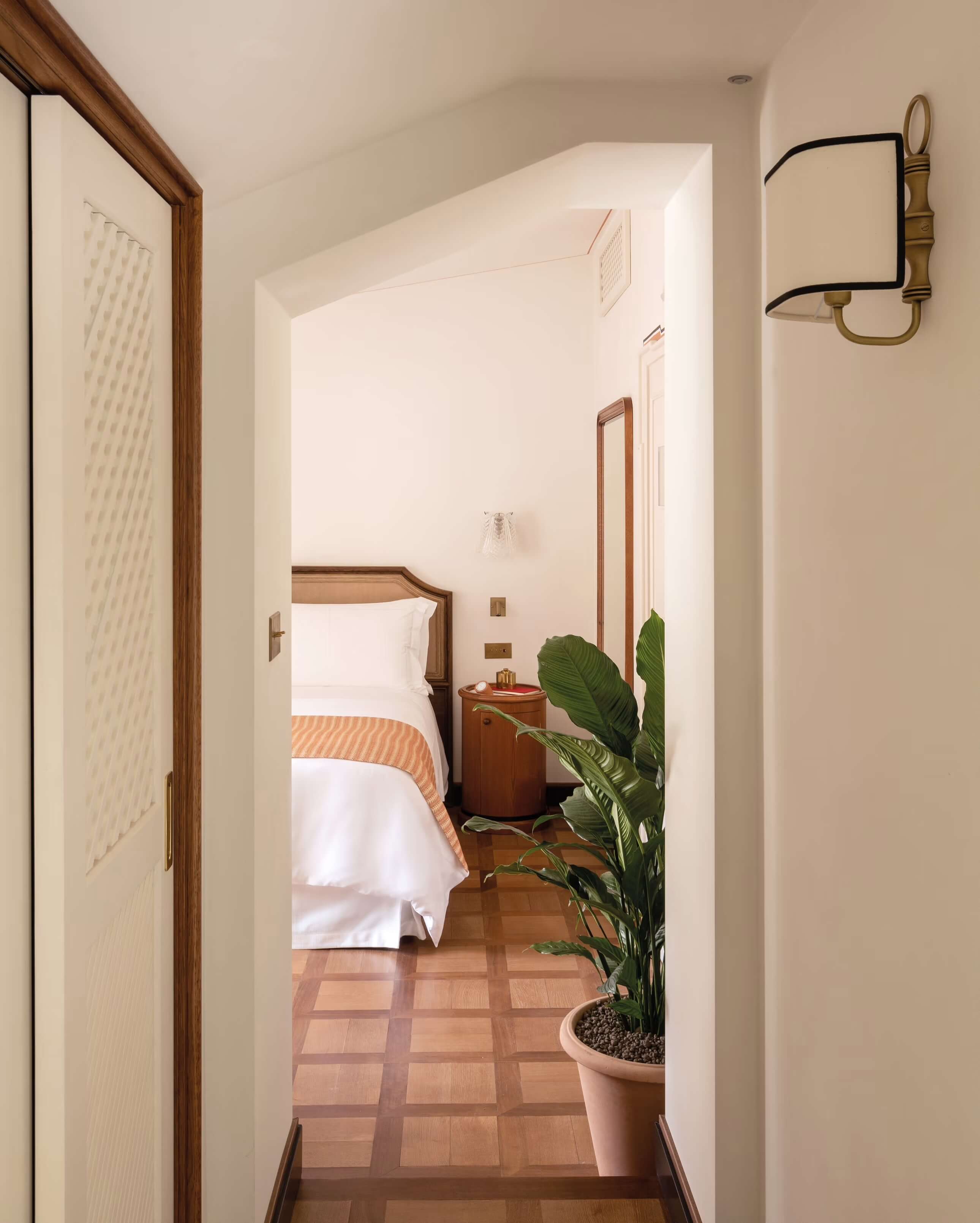 Splendido Mare, Europe — Hallway with terracotta tile flooring, wooden-framed doorway, potted plant, and glimpse of bedroom with wooden bed frame and coral striped linens.