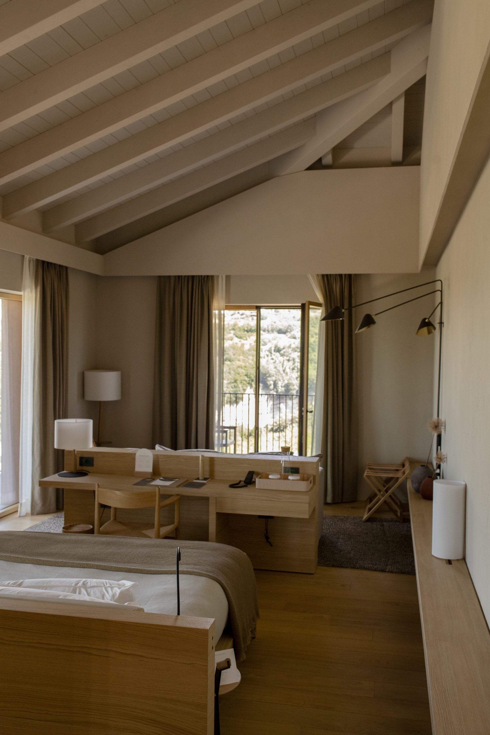 Casa di Langa, Europe — Minimalist hotel bedroom with exposed wooden beams, natural light, desk workspace, and panoramic valley views from floor-to-ceiling windows.