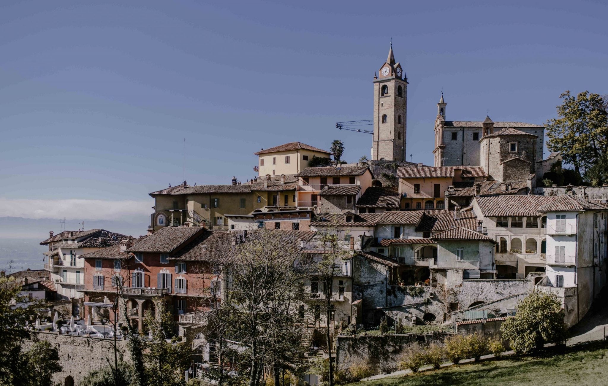 Casa di Langa, Piedmont, Italy — Medieval hilltop village with terracotta roofs, stone bell tower, and warm ochre architecture overlooking misty valleys.