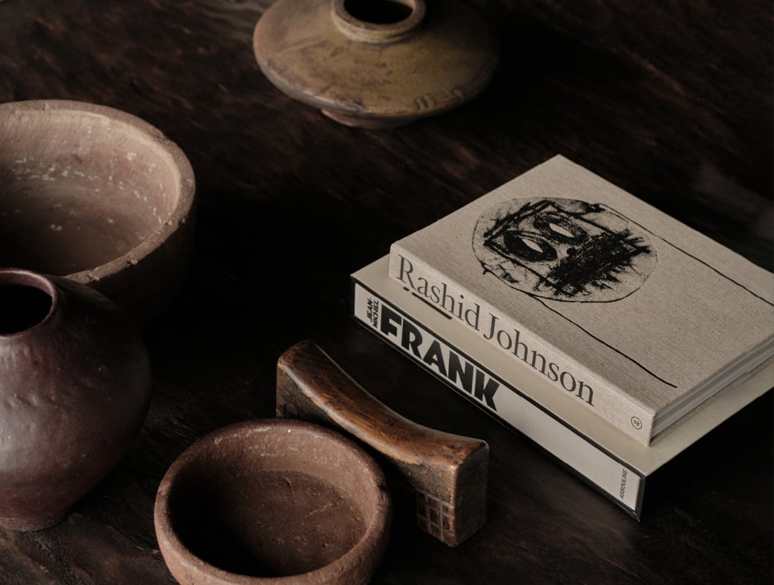 En Kyanó, Europe — Styled flatlay with ceramic vessels, wooden bowl, and Rashid Johnson "Untitled" book on dark surface, earthy textures and muted tones.
