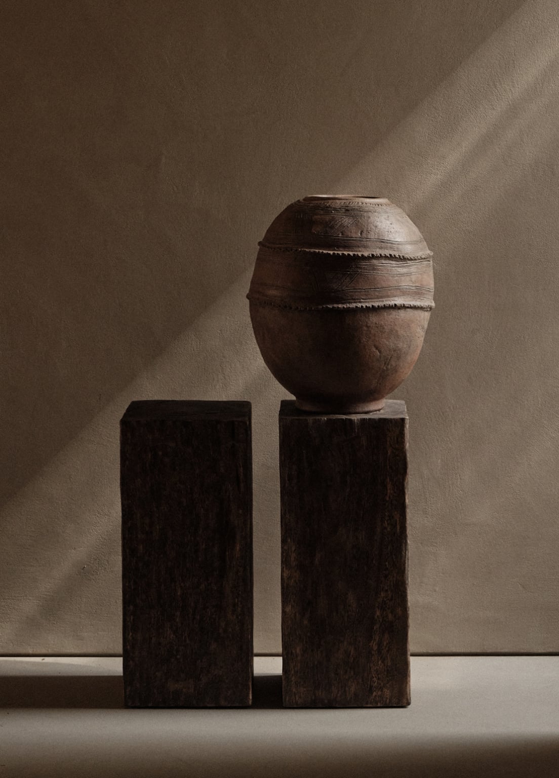 En Kyanó, Europe — Earthenware vessel with rope detailing on wooden pedestals, natural light casting shadows on neutral wall, minimalist gallery display.