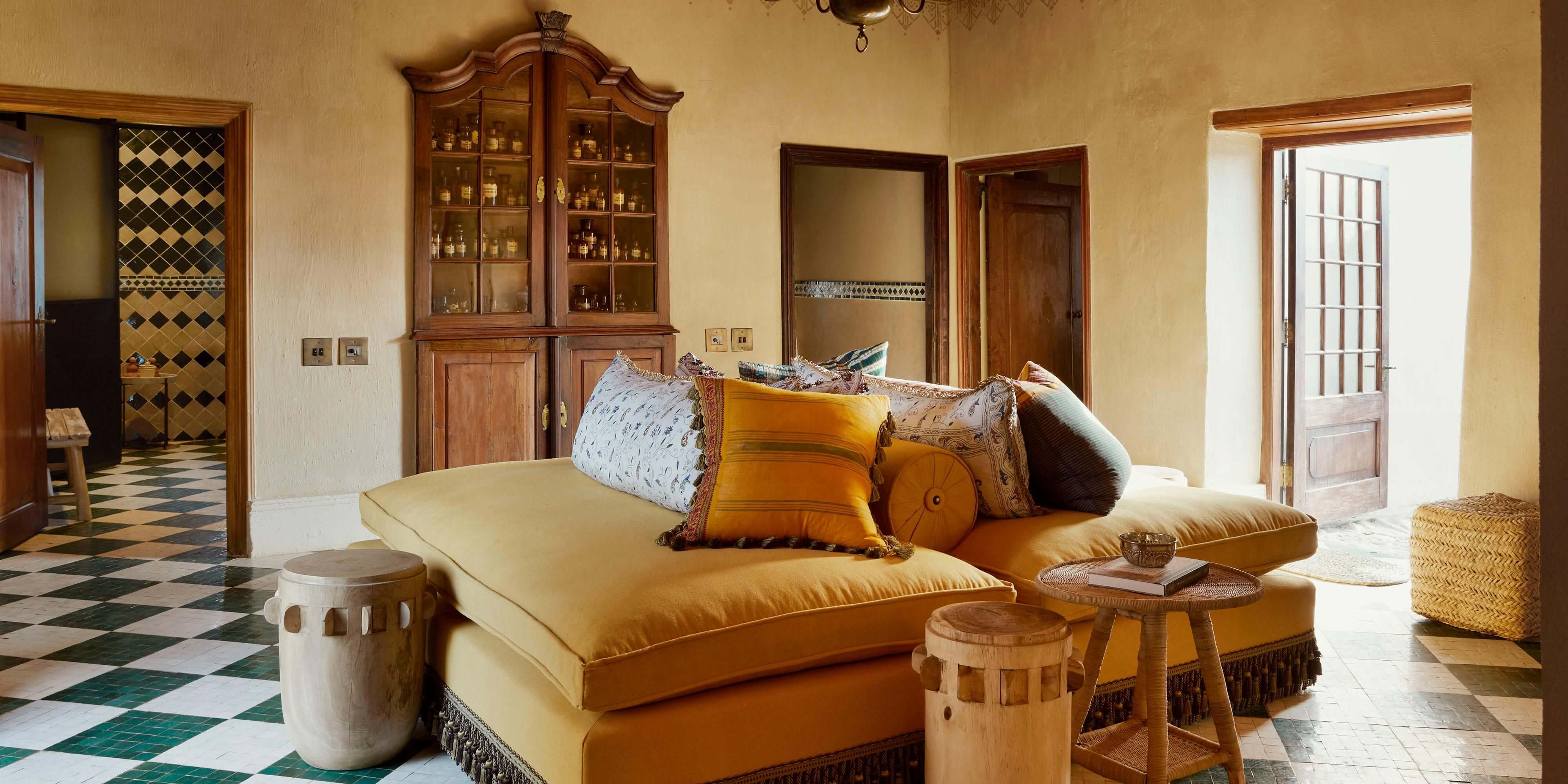 Sterrekopje, Africa — Ochre linen daybed with patterned pillows, geometric tile flooring, wooden cabinetry, and natural light in minimalist luxury interior.