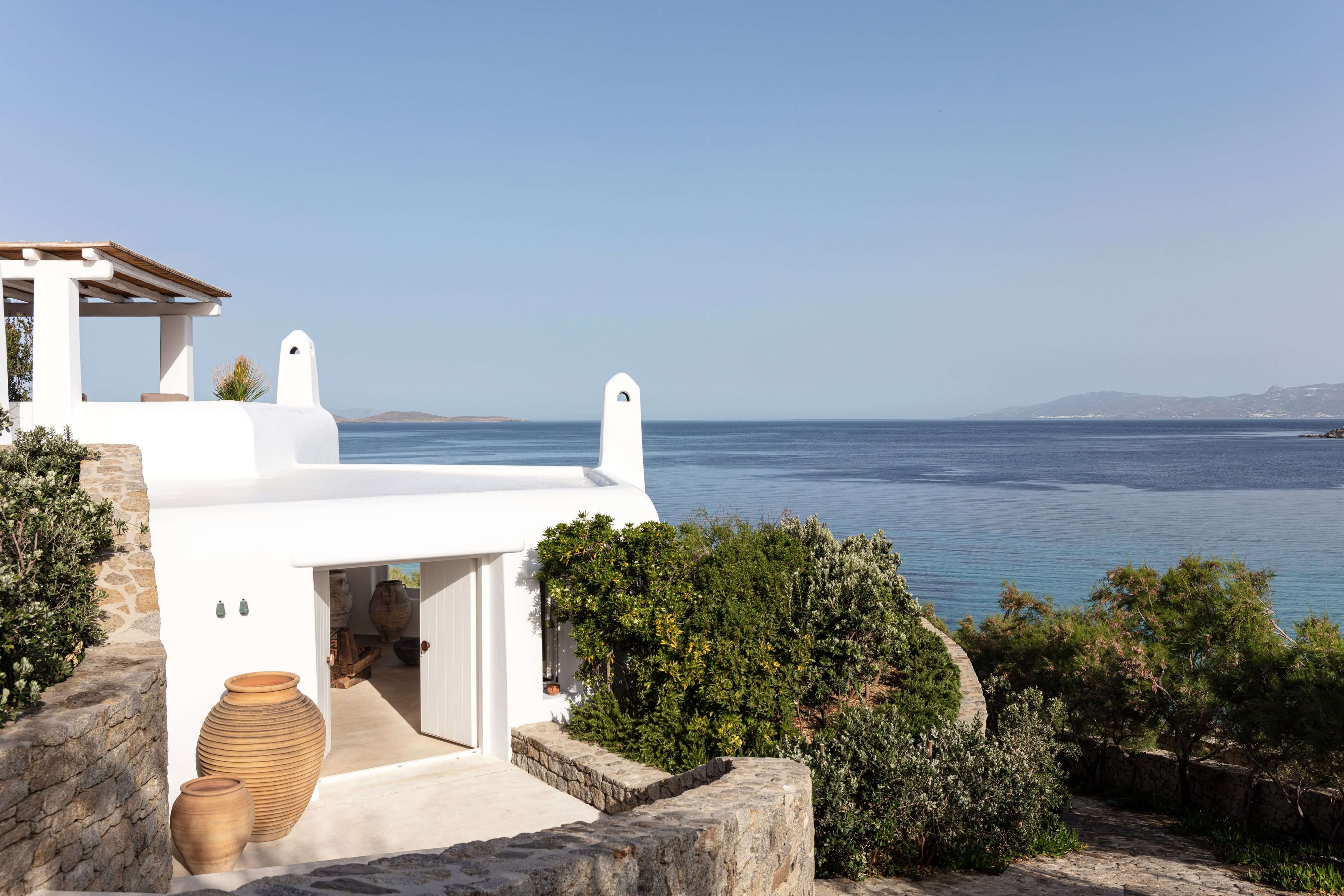 Villa Tama, Europe — Whitewashed Cycladic villa with terracotta urns, wooden pergola, and unobstructed sea views overlooking the Aegean from a sun-drenched clifftop terrace.