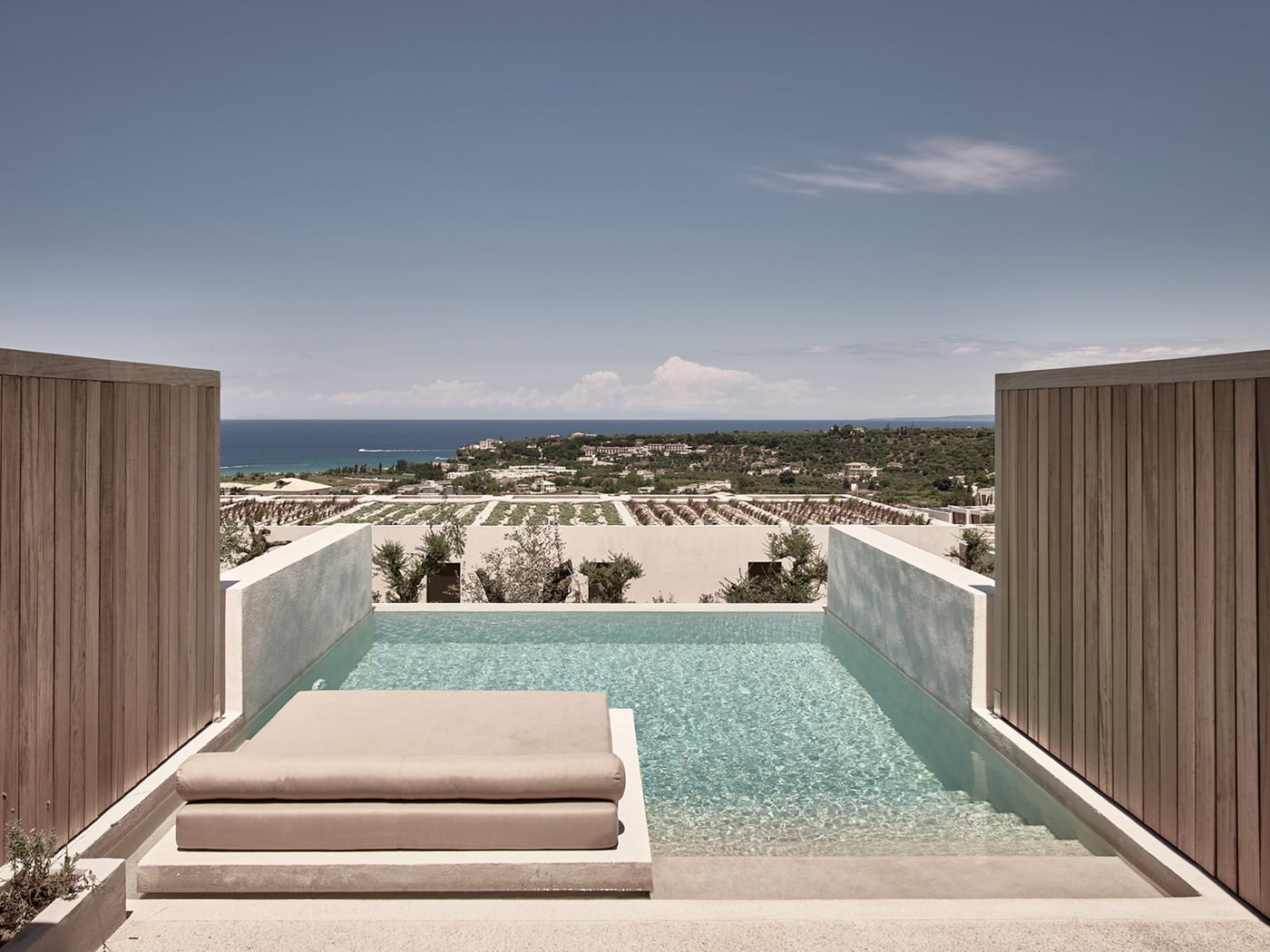 Olea All Suite Hotel, Europe — Minimalist poolside terrace with concrete lounger, turquoise water, sea views, and olive groves beyond.