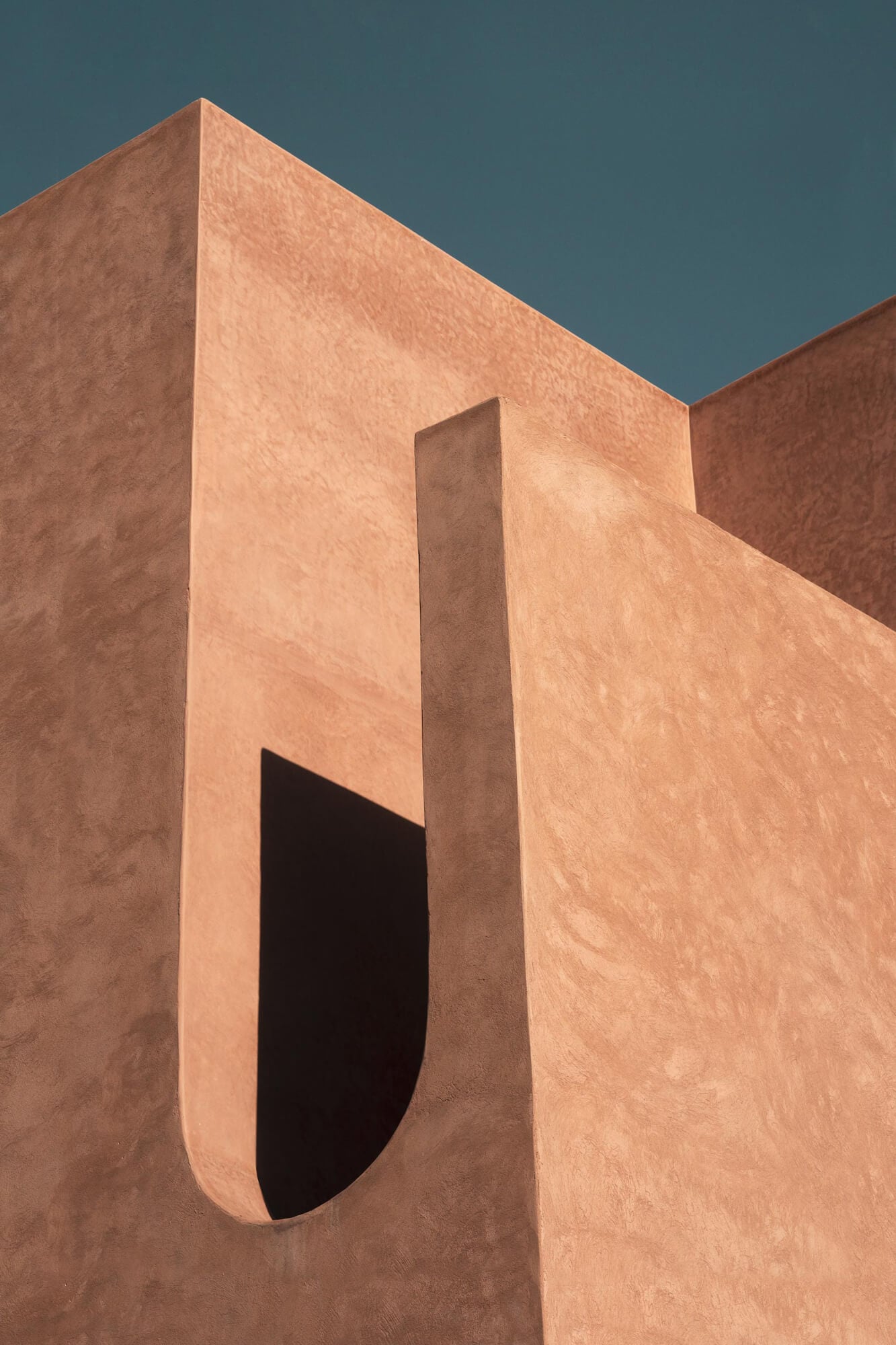 Maison Brummell Majorelle, Africa — Terracotta stucco facade with geometric arch doorway and sharp shadows against clear sky, modernist hospitality architecture.