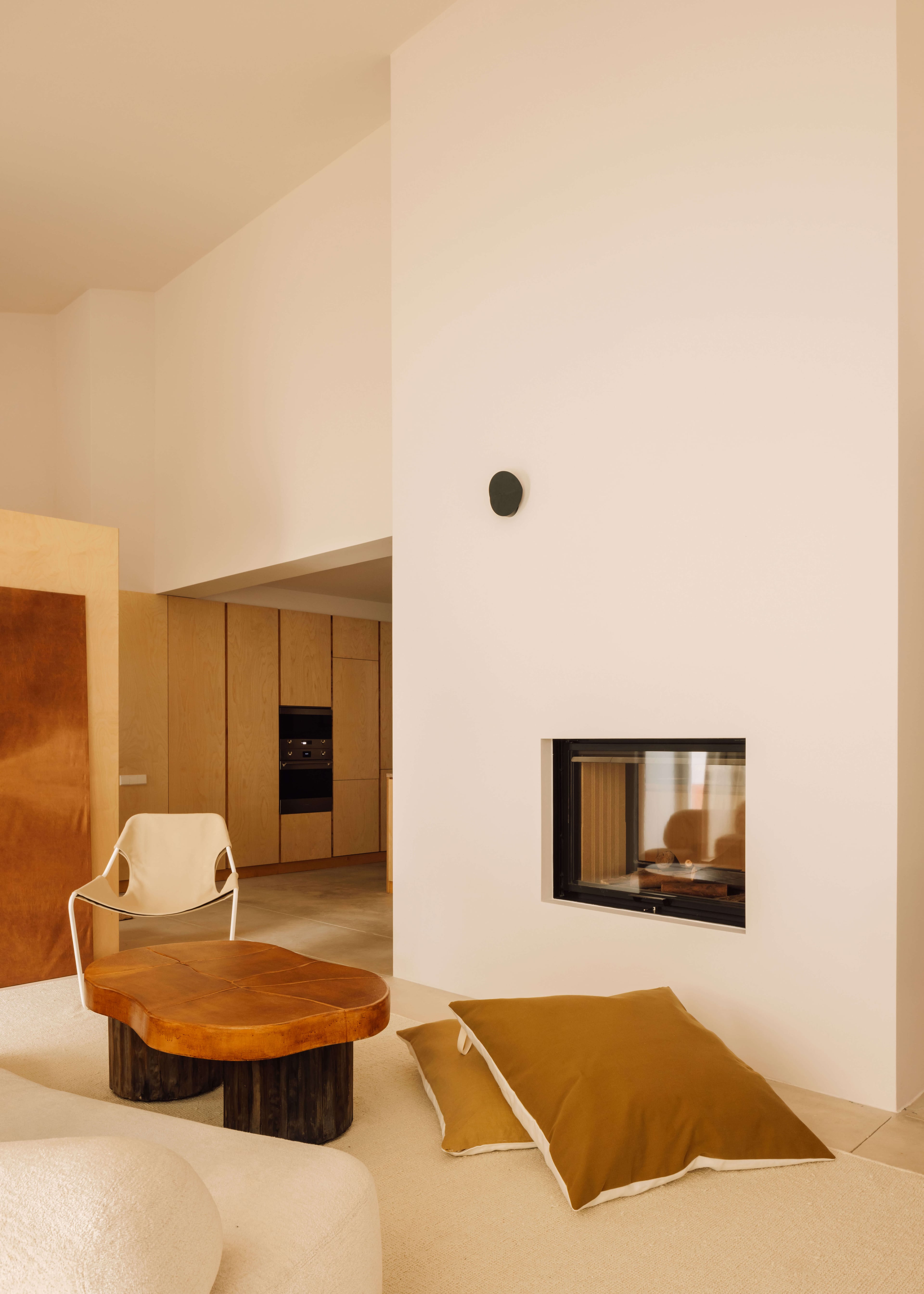Casa Quatro, Europe — Minimalist living room with warm wood furnishings, white walls, built-in fireplace, and natural light from skylights.