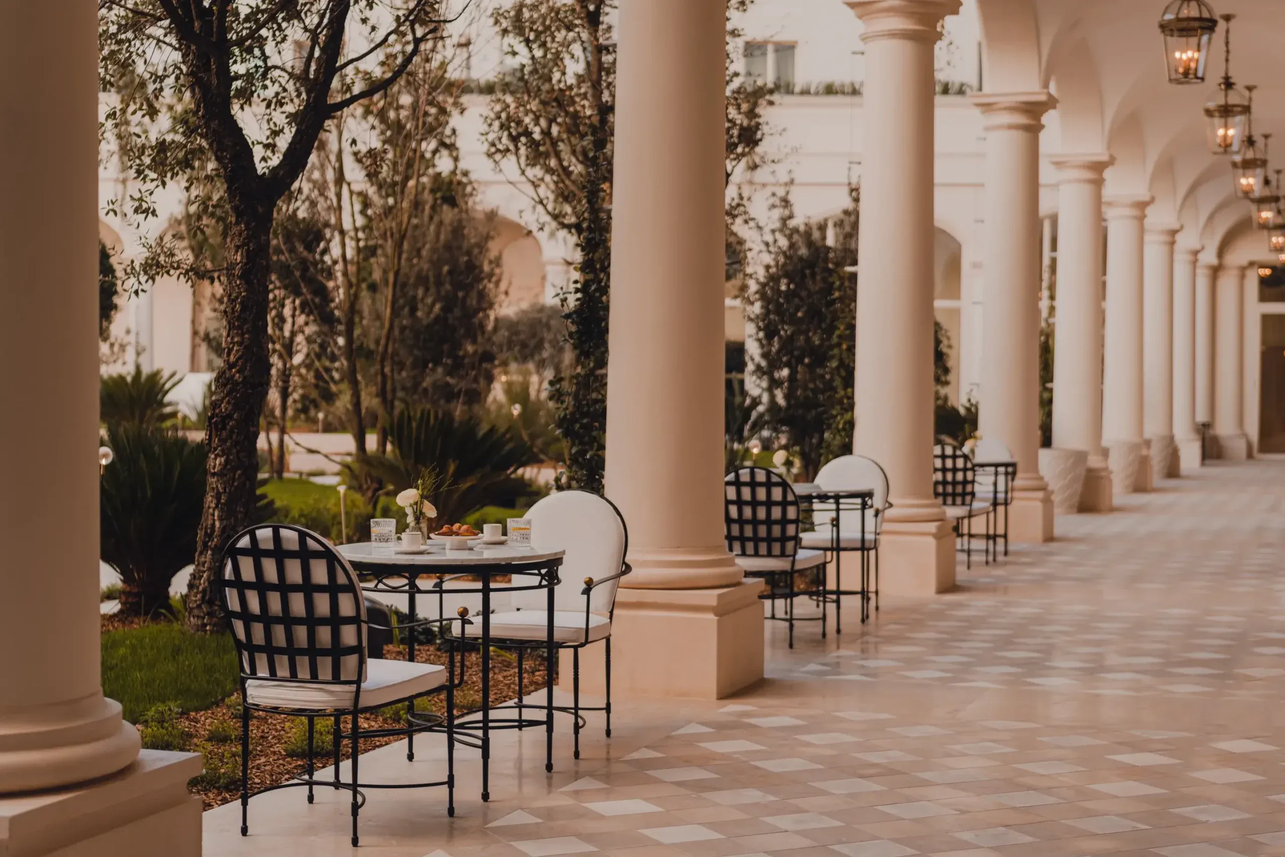 Carlton Cannes, Cannes, France — Colonnade terrace with black lattice chairs, white cushions, and manicured gardens under warm afternoon light.