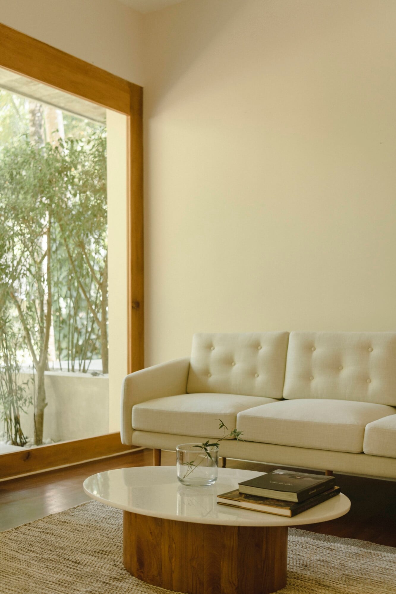 Kurulu Bay, Asia — Minimalist living room with cream linen sofa, oval marble coffee table, wooden frame window overlooking bamboo garden, natural light, neutral palette.