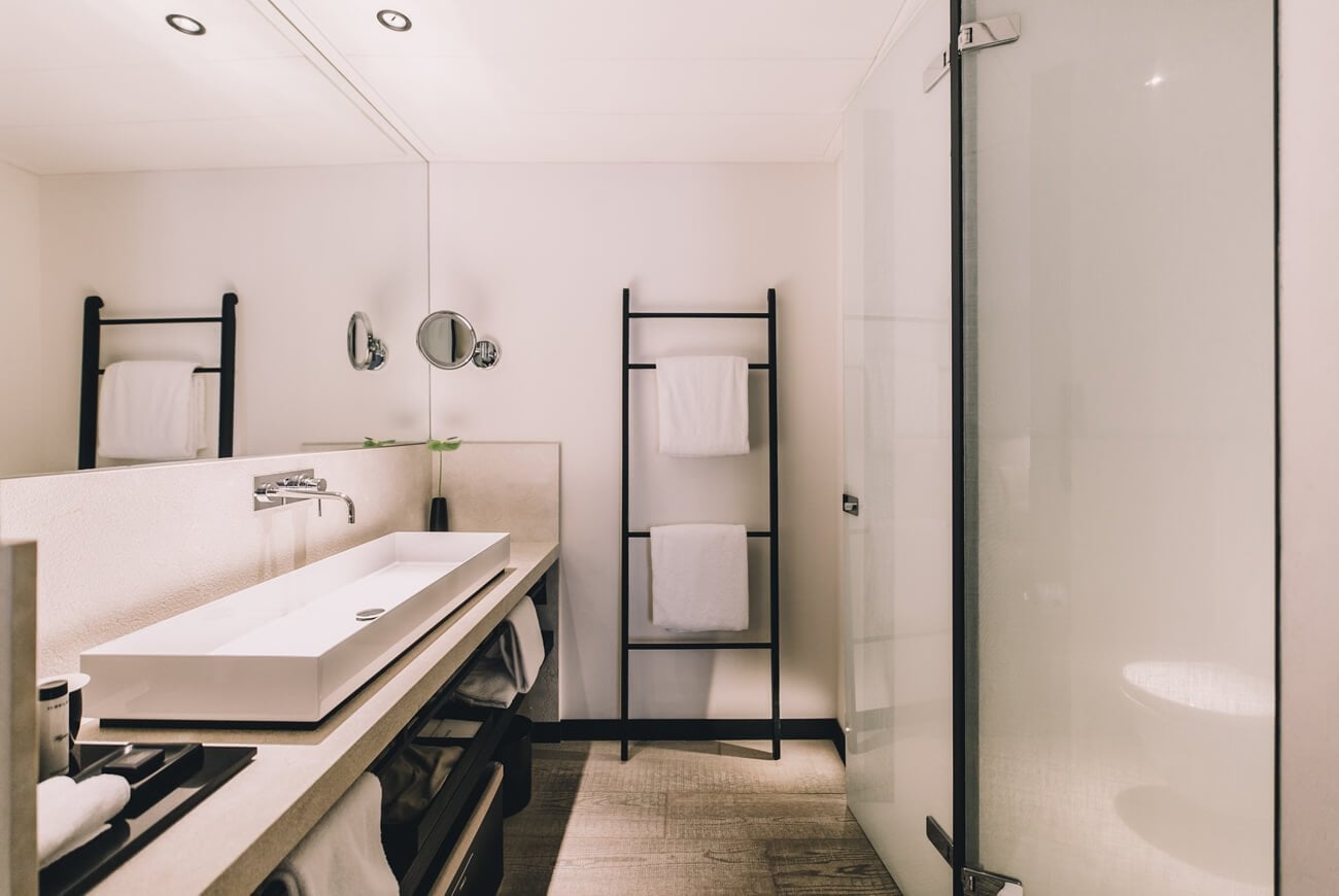 Sant Francesc Hotel Singular, Balearic Islands — Minimalist bathroom with floating concrete sink, black metal towel ladders, and frameless glass shower enclosure.
