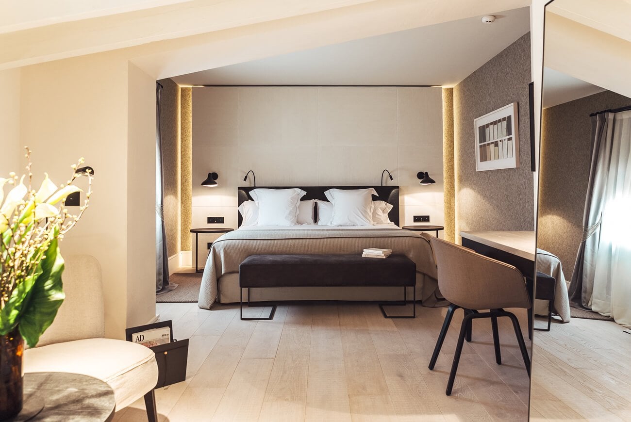 Sant Francesc Hotel Singular, Balearic Islands, Spain — Modern luxury suite with illuminated alcove bed, warm wood flooring, textured taupe walls, and contemporary minimalist furnishings.