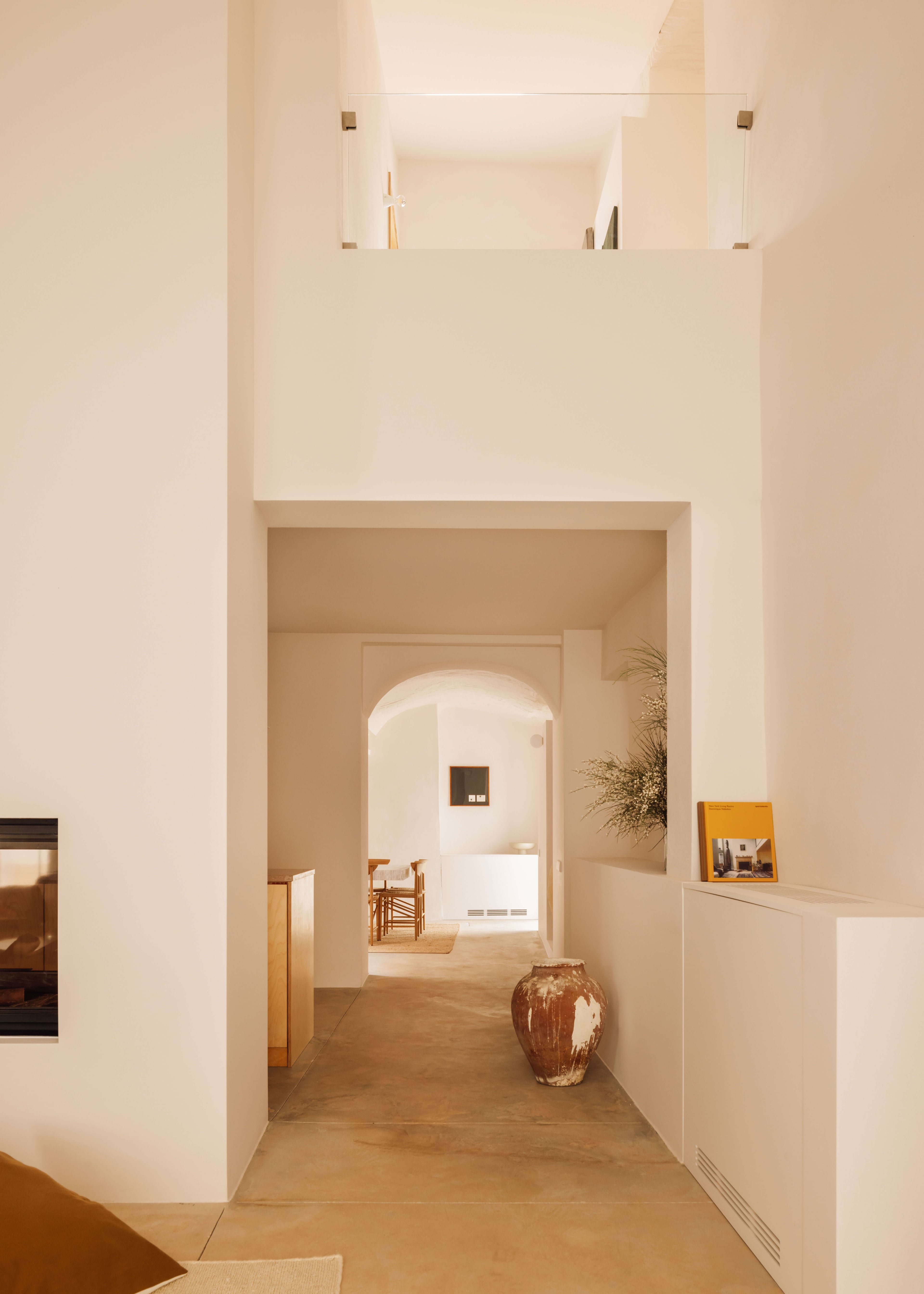 Casa Quatro, Europe — Minimalist corridor with arched doorway, skylights, terracotta vessel, warm wooden flooring and cream-white walls creating serene Mediterranean interiors.