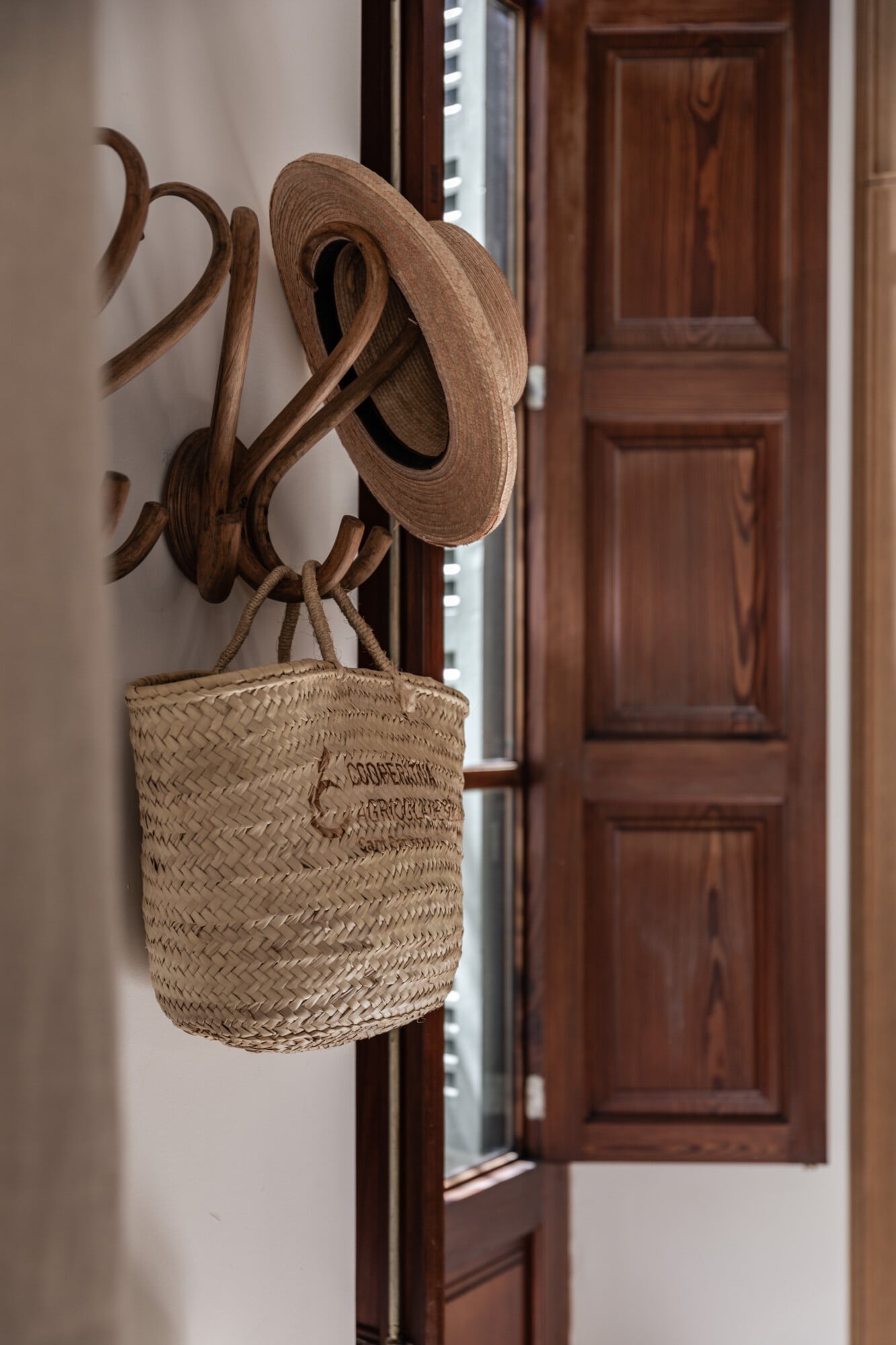 Mon Cor, Balearic Islands — Wooden sculptural hat rack with woven straw basket, rustic coastal interior design detail.